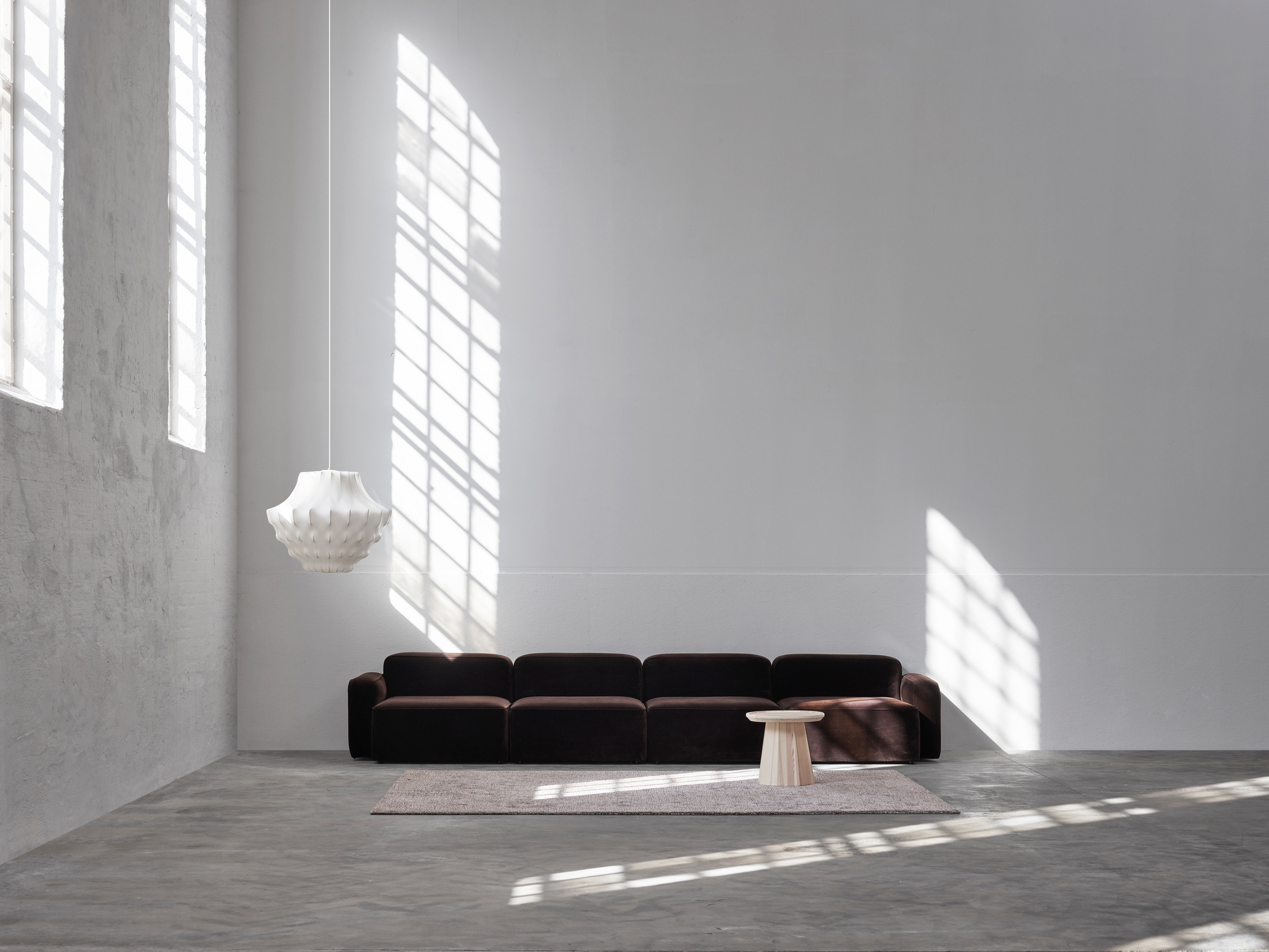 Weiße Phantom Lampe von Normann Copenhagen über braunem Sofa in minimalistischem Raum mit Tageslicht.