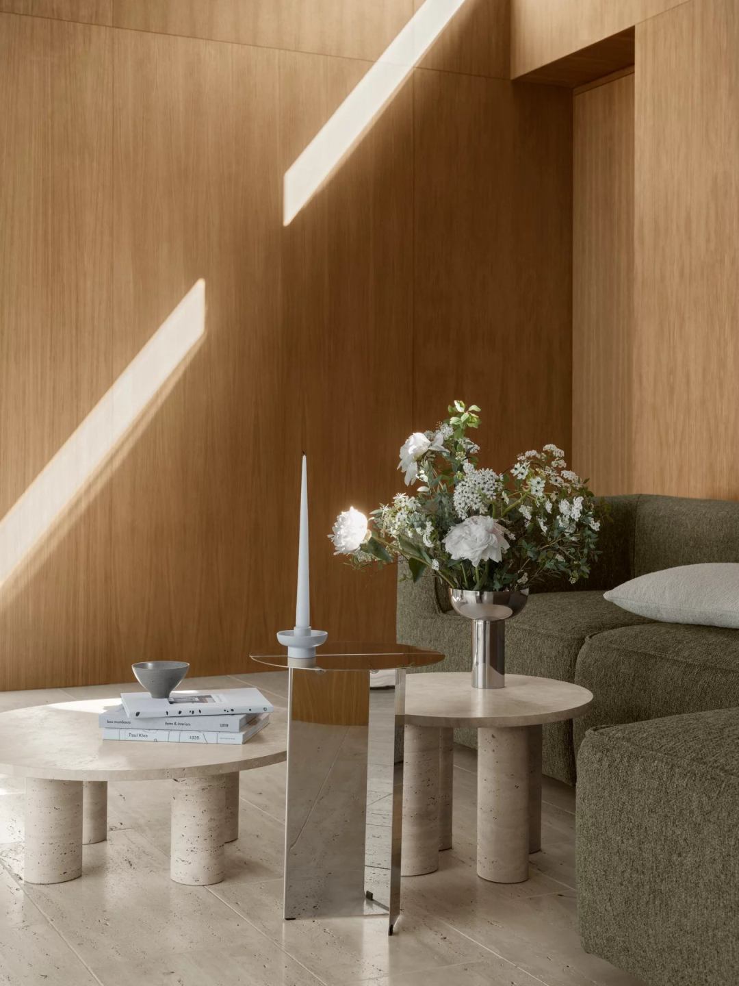 Blomus Volos Couchtisch aus Travertin, rund, mit Büchern, Kerze und Blumen aufgestellt.