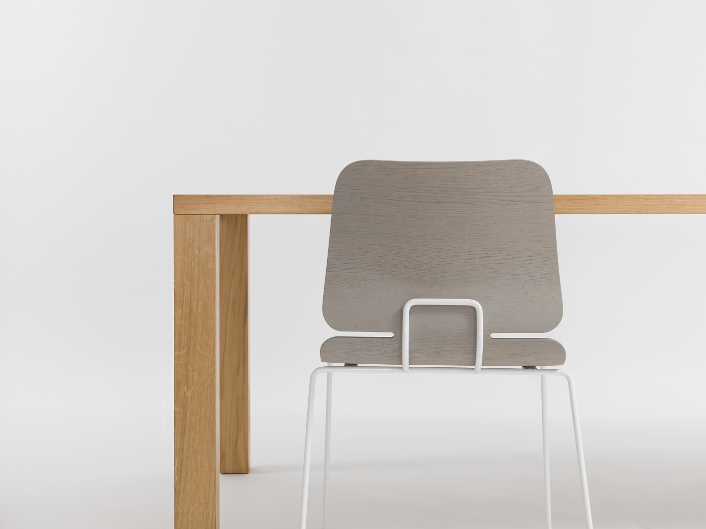 Pjur Esstisch Zeitraum: Detailansicht von Tischbein aus hellem Holz und Stuhl mit grauem Holzsitz.