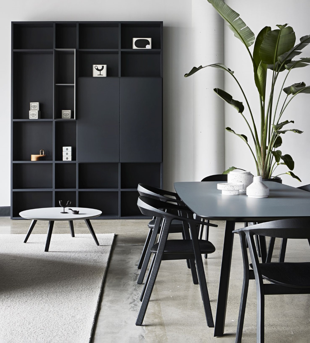 Modernes Esszimmer mit grauem Esstisch, schwarzen Stühlen, Bücherregal und Beistelltisch auf einem Teppich.