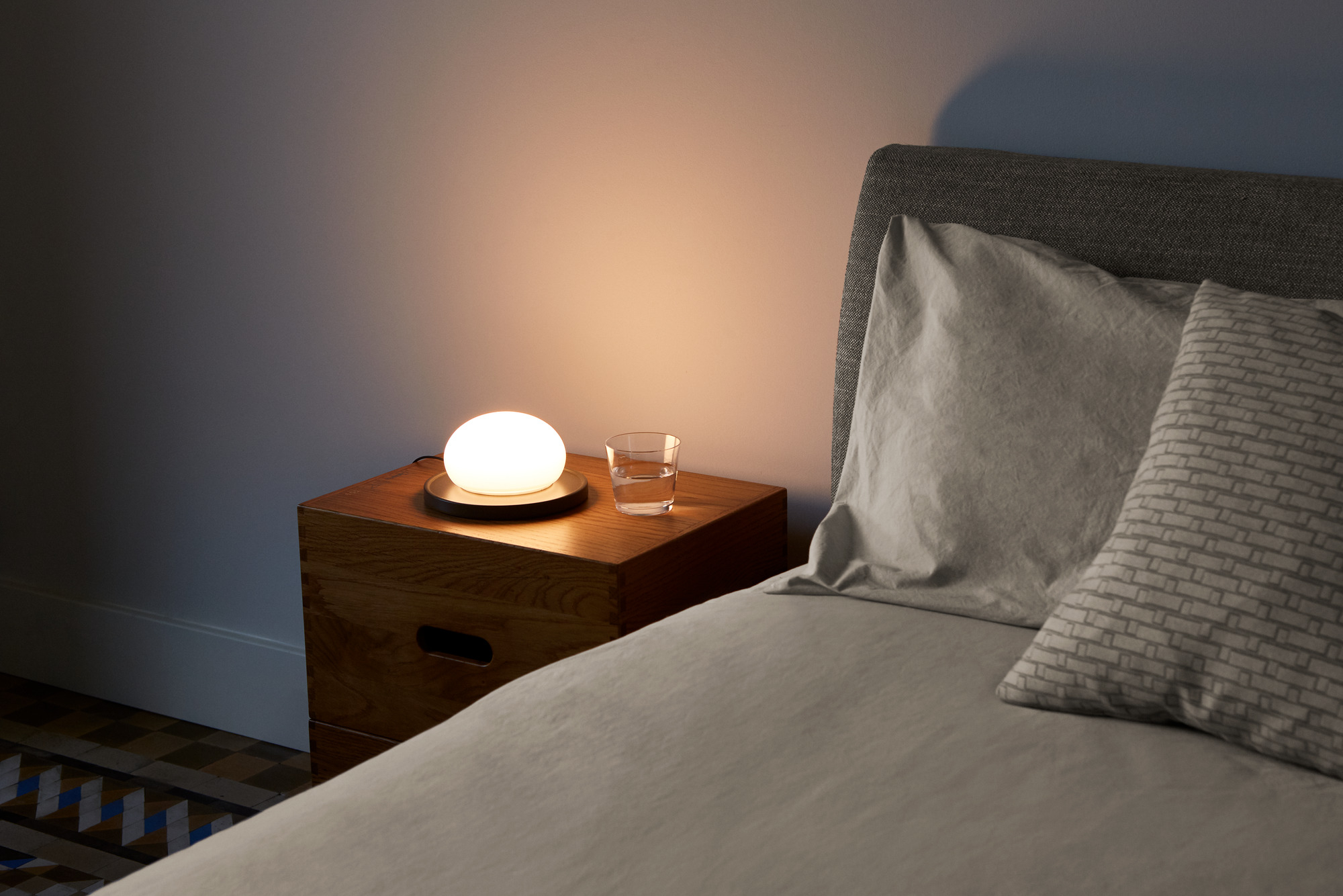 Weiße Bolita Tischleuchte von Marset auf Nachttisch neben Bett mit Kissen. LED Lampe.