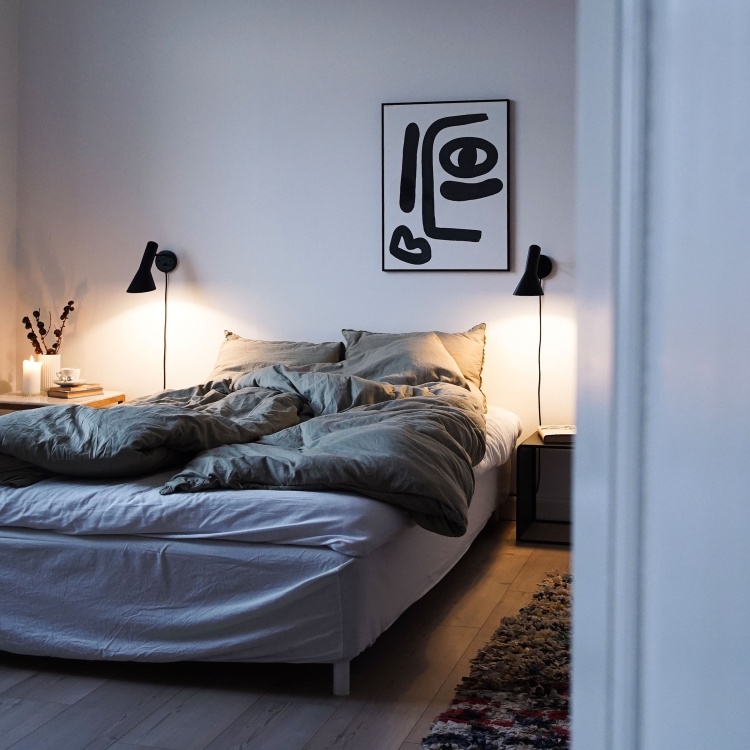 Schlafzimmer mit Bett und zwei schwarzen AJ Wandleuchten von Louis Poulsen als Nachttischlampen.