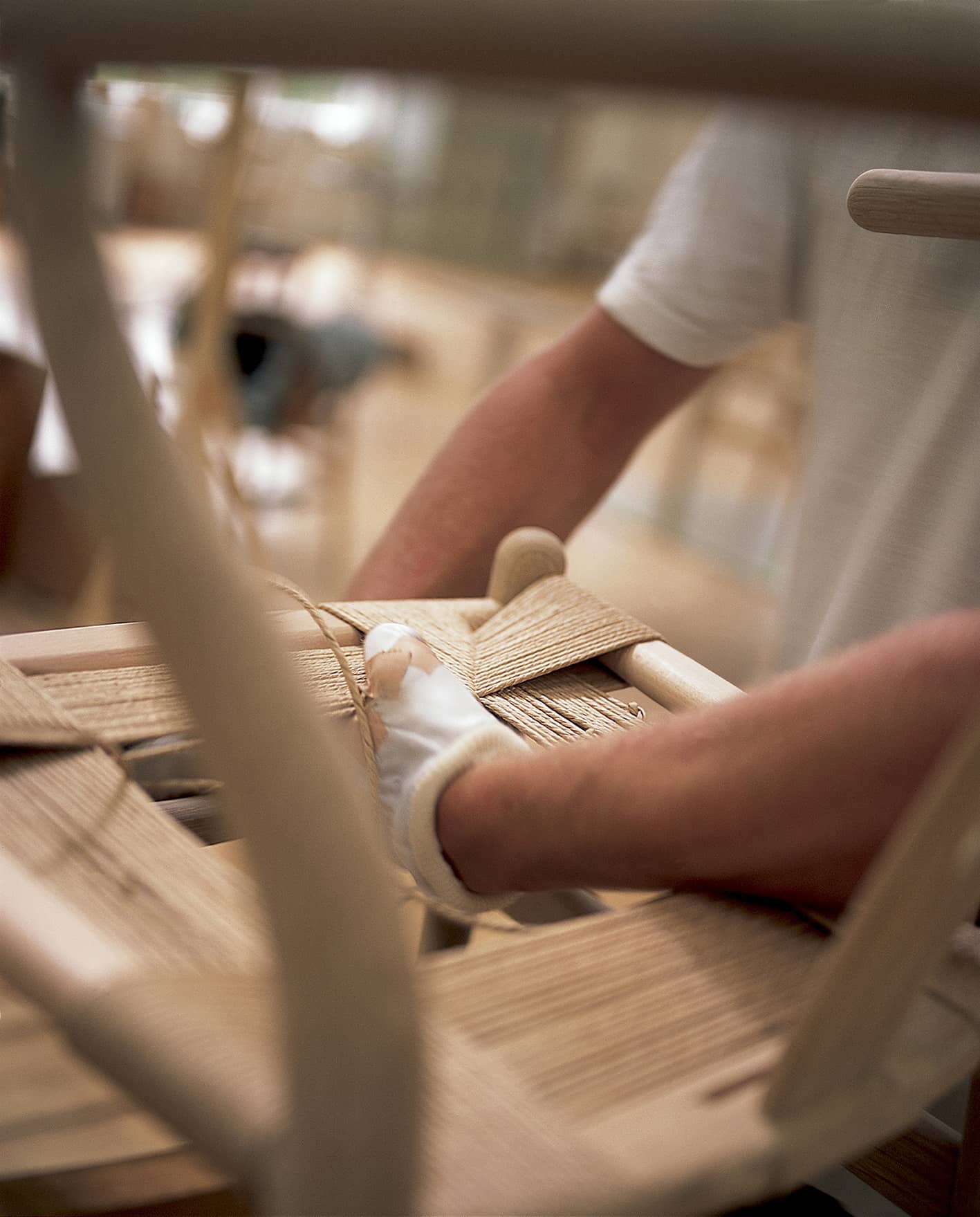Handwerker flechtet Sitzfläche eines Holzstuhls mit Papierkordel, traditionelle Stuhlreparatur und Möbelrestaurierung.