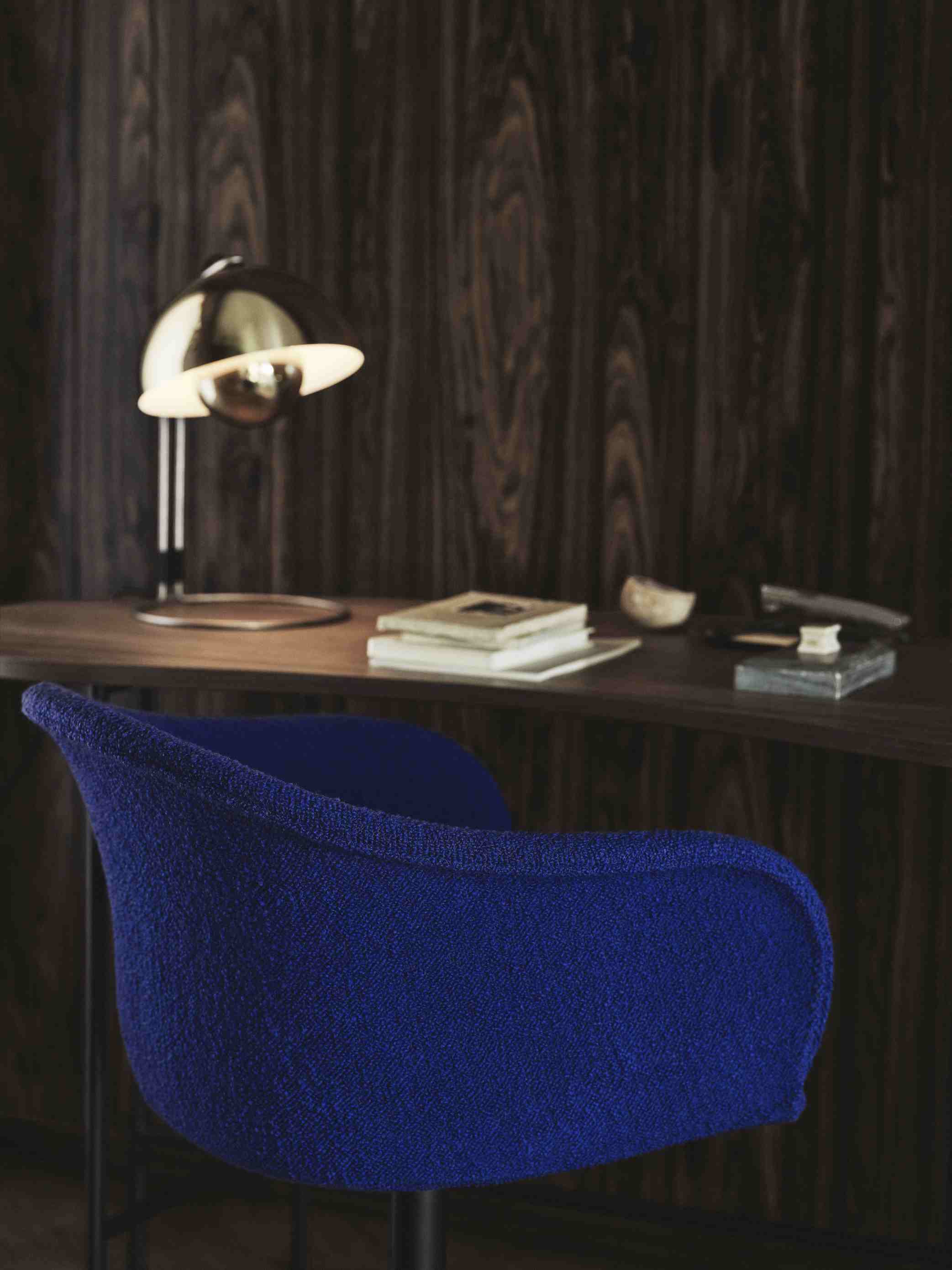 AndTradition Palette Schreibtisch mit Lampe und blauem Stuhl vor dunkler Holzvertäfelung, Bücher und Dekoration.