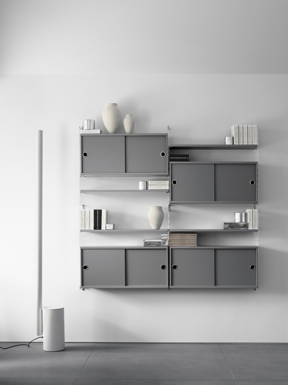 Graues String Regal-System "Wohnzimmer KONFIGURATIONEN L2" mit Schiebetüren und Dekorationsartikeln an weißer Wand.