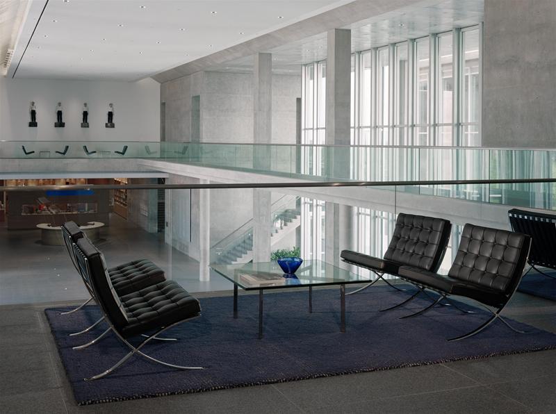Barcelona Couchtisch aus Kristallglas von Knoll International mit schwarzen Barcelona Sesseln auf blauem Teppich.
