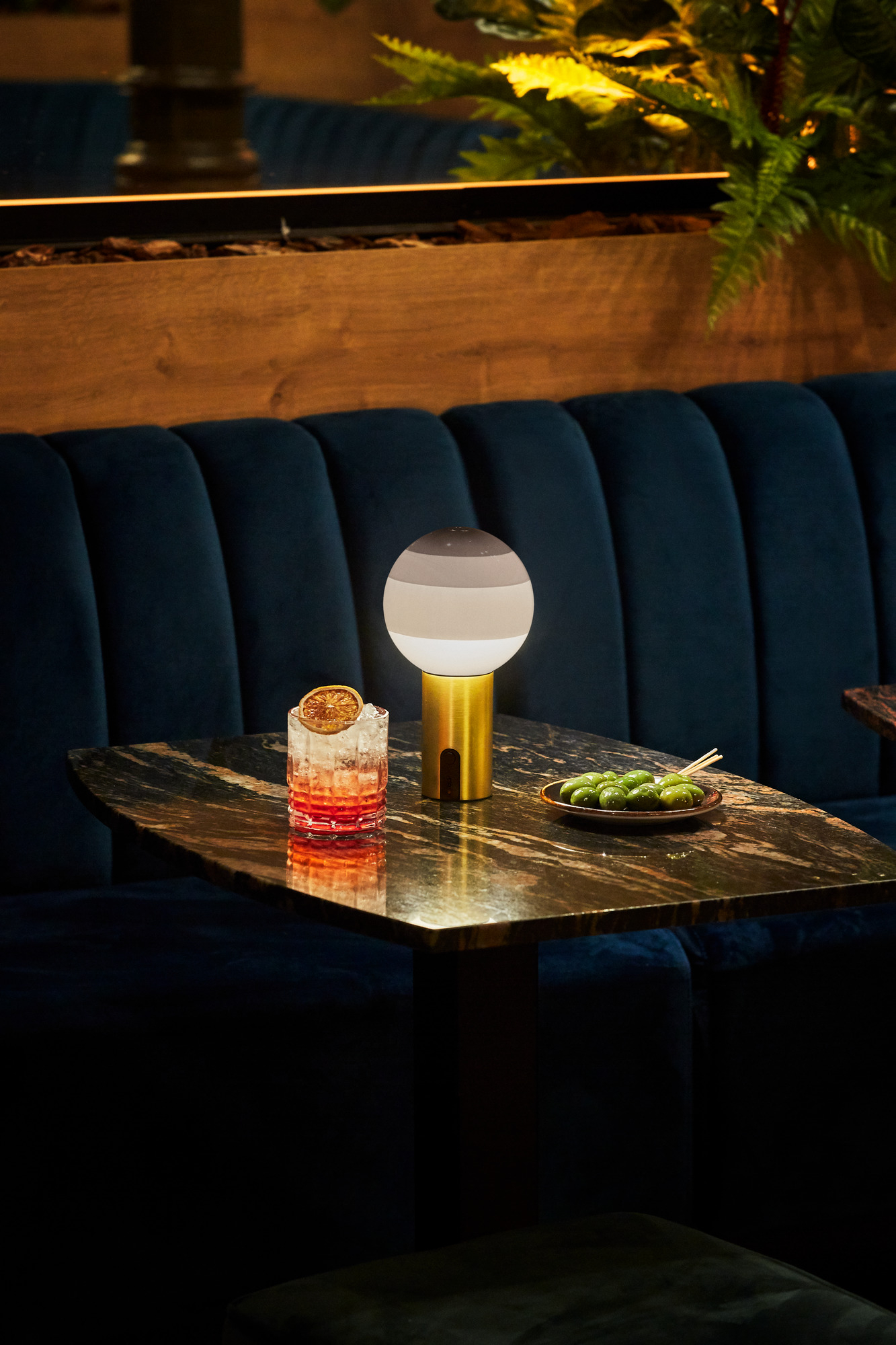 Marset Dipping Light Portable LED Akkuleuchte auf Tisch mit Cocktail und Oliven.