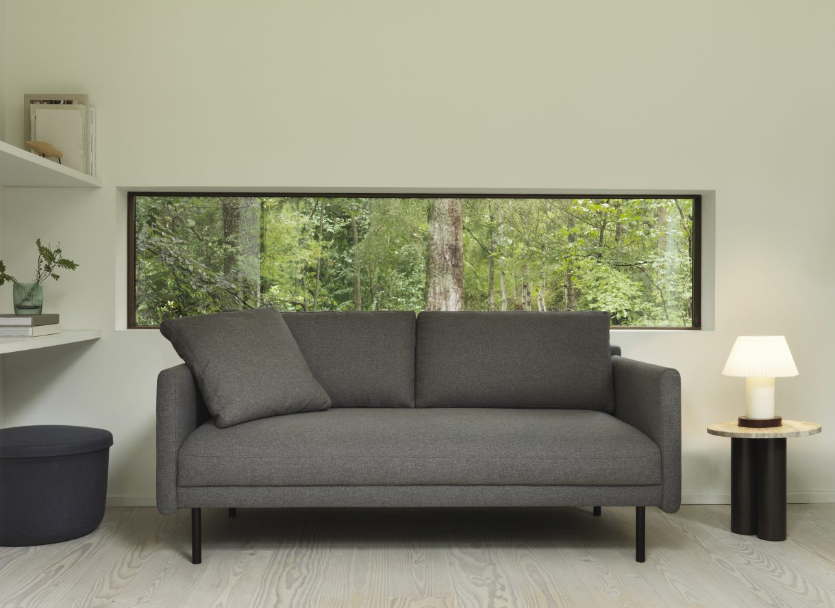 Graues Sofa mit Kissen und Normann Copenhagen Dit Coffee Table Beistelltisch im modernen Wohnzimmer mit Waldblick.