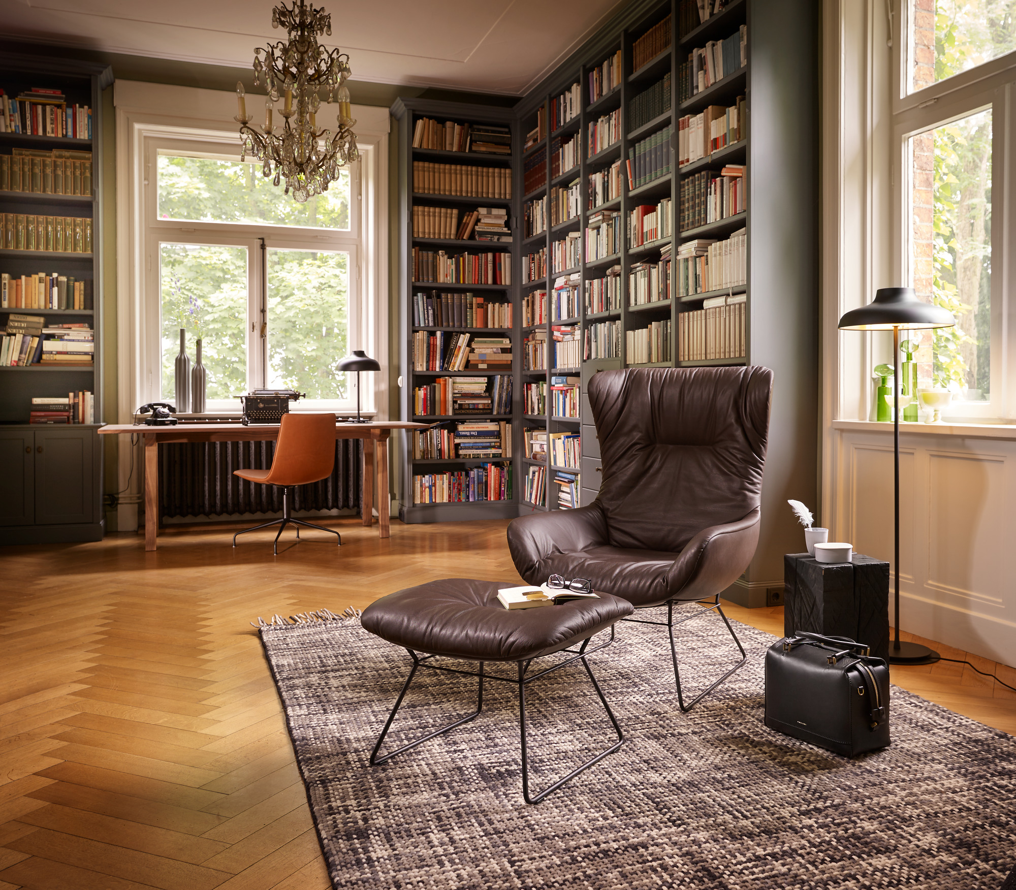 Leder Ohrensessel Leya Wingback von Freifrau Manufaktur mit Hocker in stilvollem Arbeitszimmer mit Bücherregal.