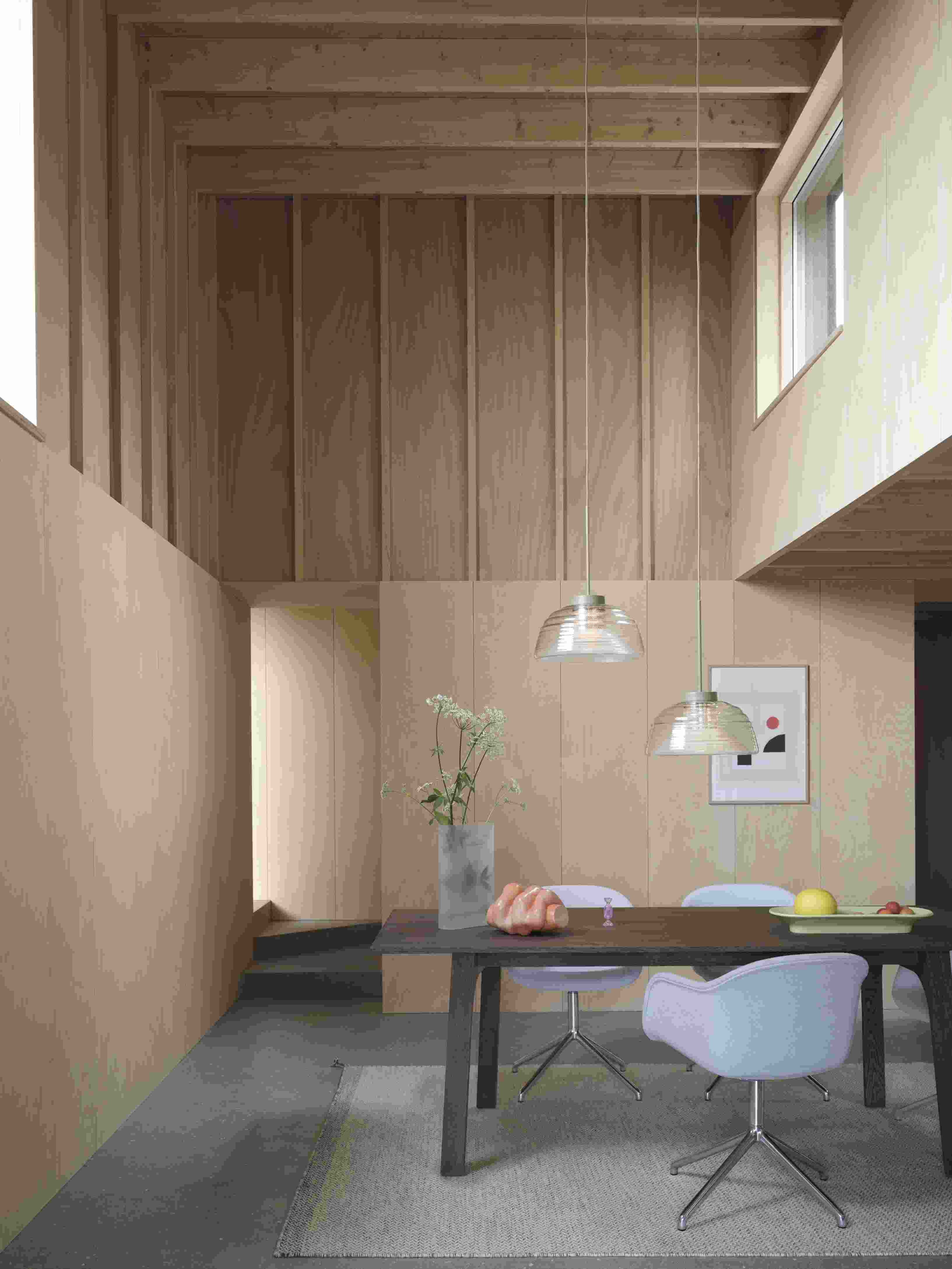 Esszimmer mit Muuto Two-Layer Pendelleuchten, Esstisch, Stühlen und Holzwänden für moderne Innenarchitektur.