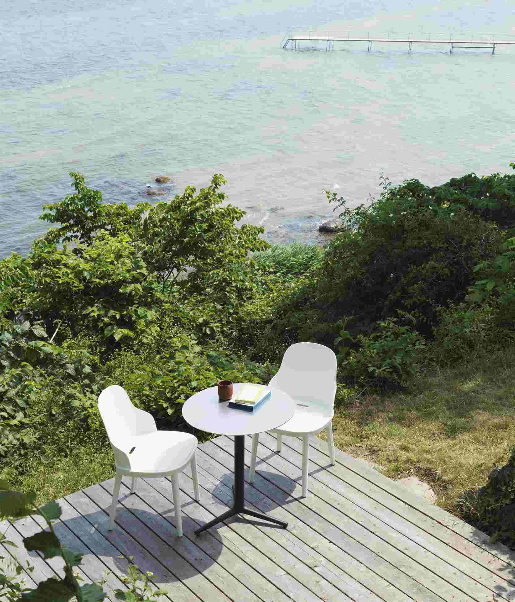Zwei weiße Allez Chair Stühle von Normann Copenhagen mit kleinem Tisch auf Holzterrasse am Meer.