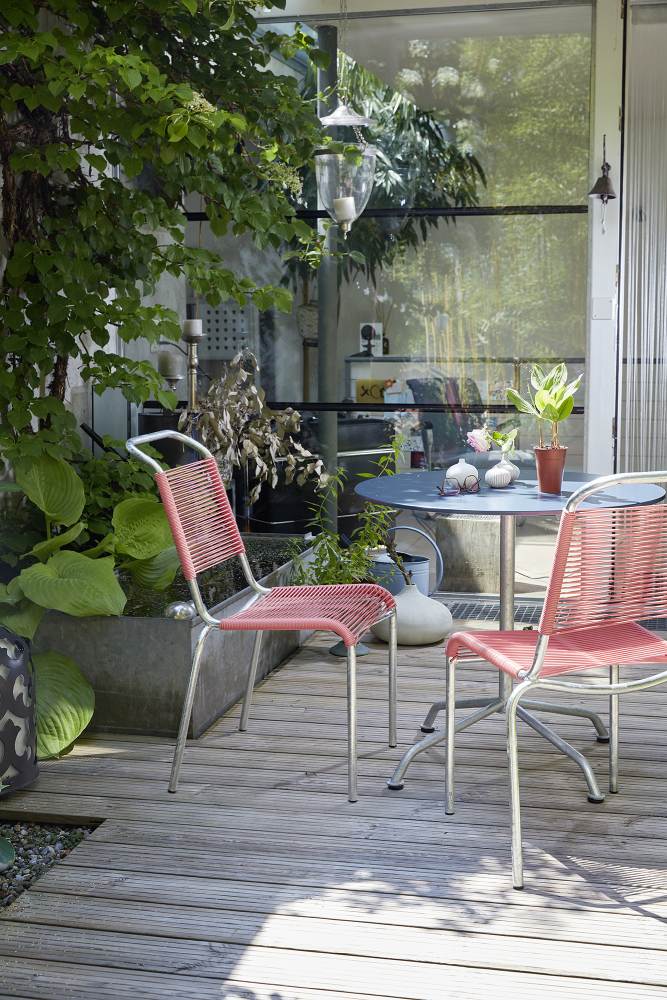 Zwei rote Altorfer Stühle Outdoor auf einer Holzterrasse mit Tisch und Pflanzen.