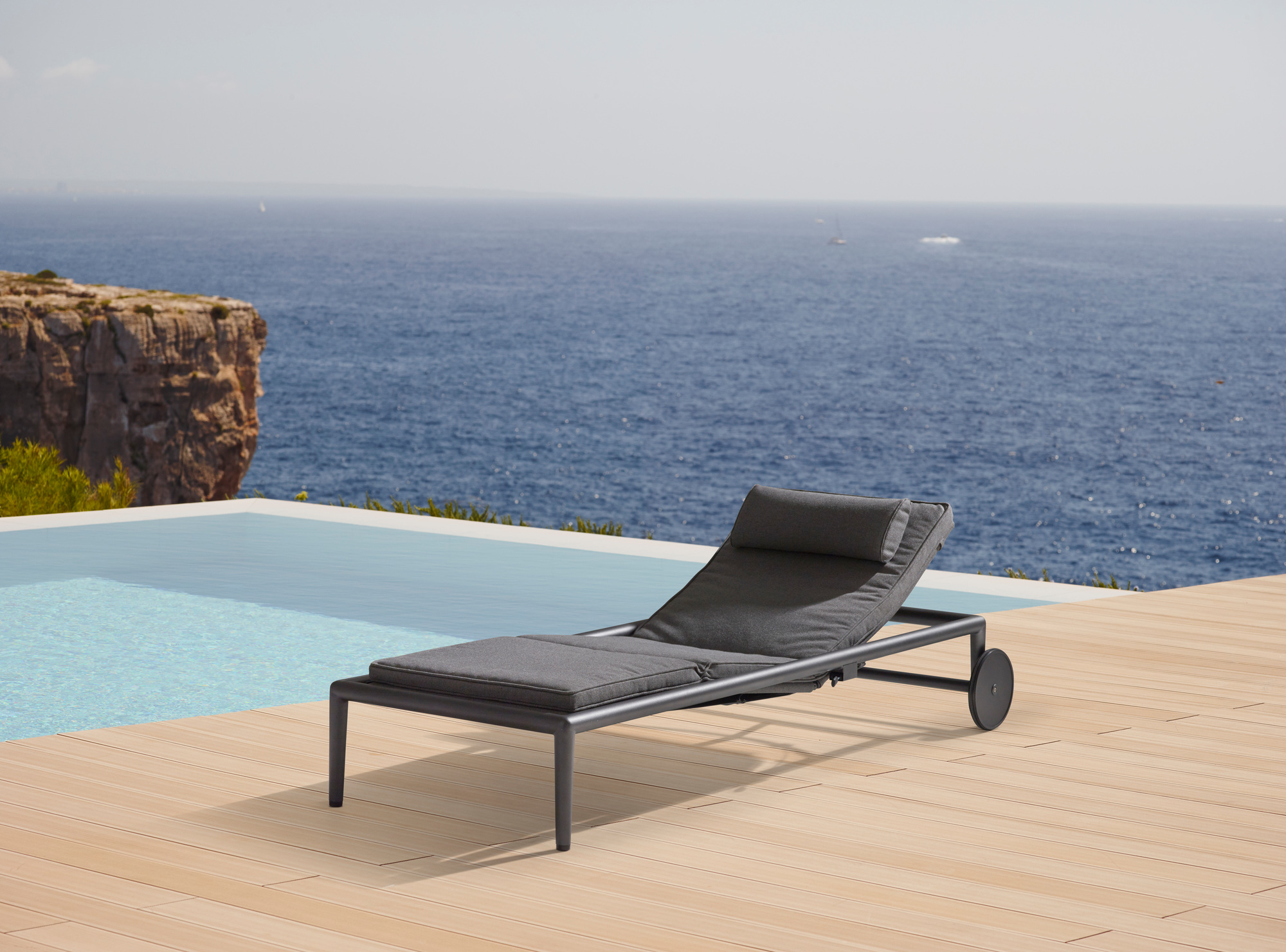 Cane-Line Conic Sonnenliege Outdoor mit grauen Polstern am Pool mit Meerblick.