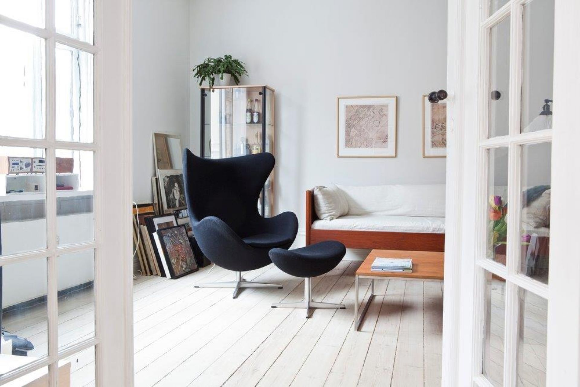 Wohnzimmer mit schwarzem Egg Chair Sessel und Hocker auf weißem Holzboden, skandinavisches Design.