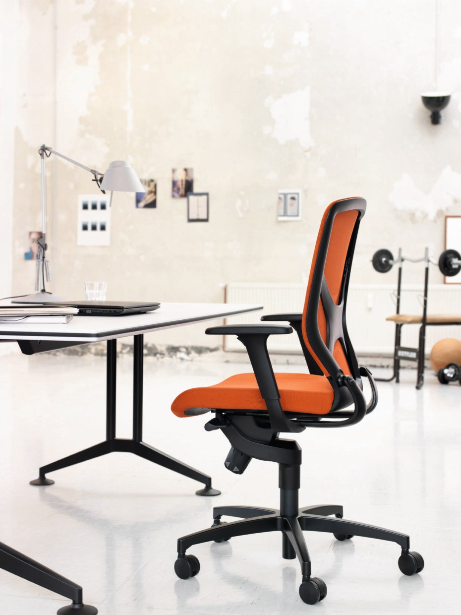 Oranger Bürostuhl mit schwarzem Gestell und Rollen vor einem Schreibtisch in modernem Büro.