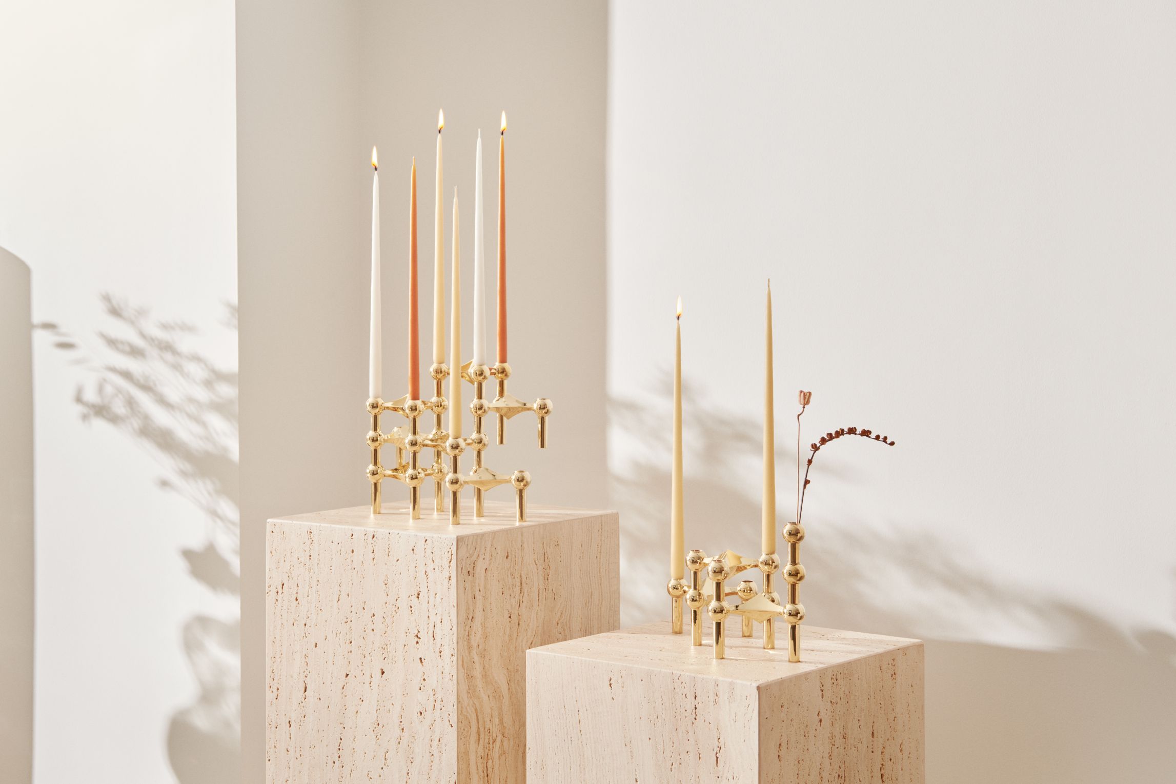 Kerzenständer Set aus Messing mit Kerzen und dekorativer Pflanze auf beigen Sockeln.