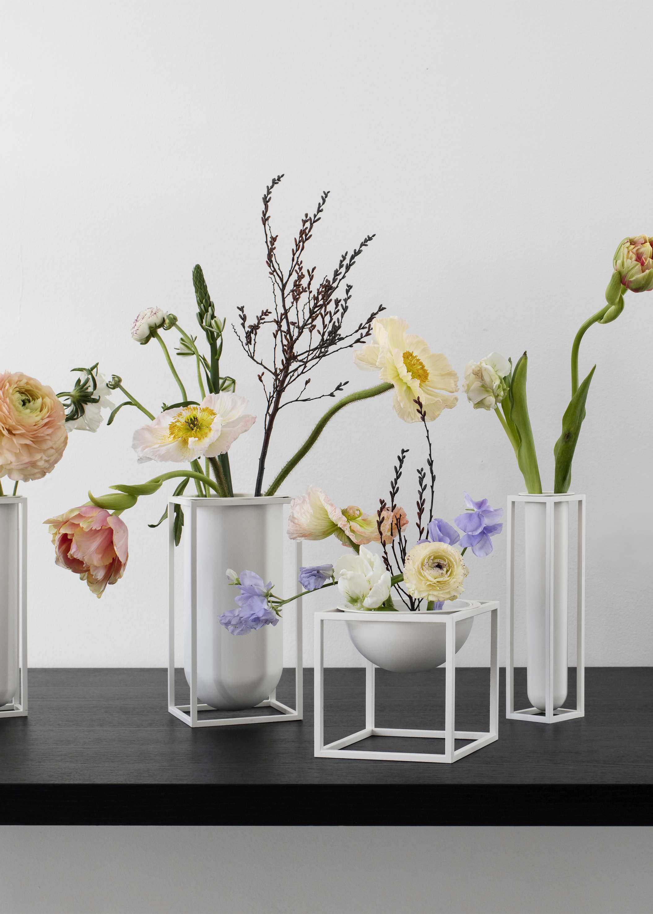 Blumenarrangements in weißen Designervasen auf schwarzem Tisch. Moderne Blumendekoration mit Ranunkeln, Tulpen und Zweigen.