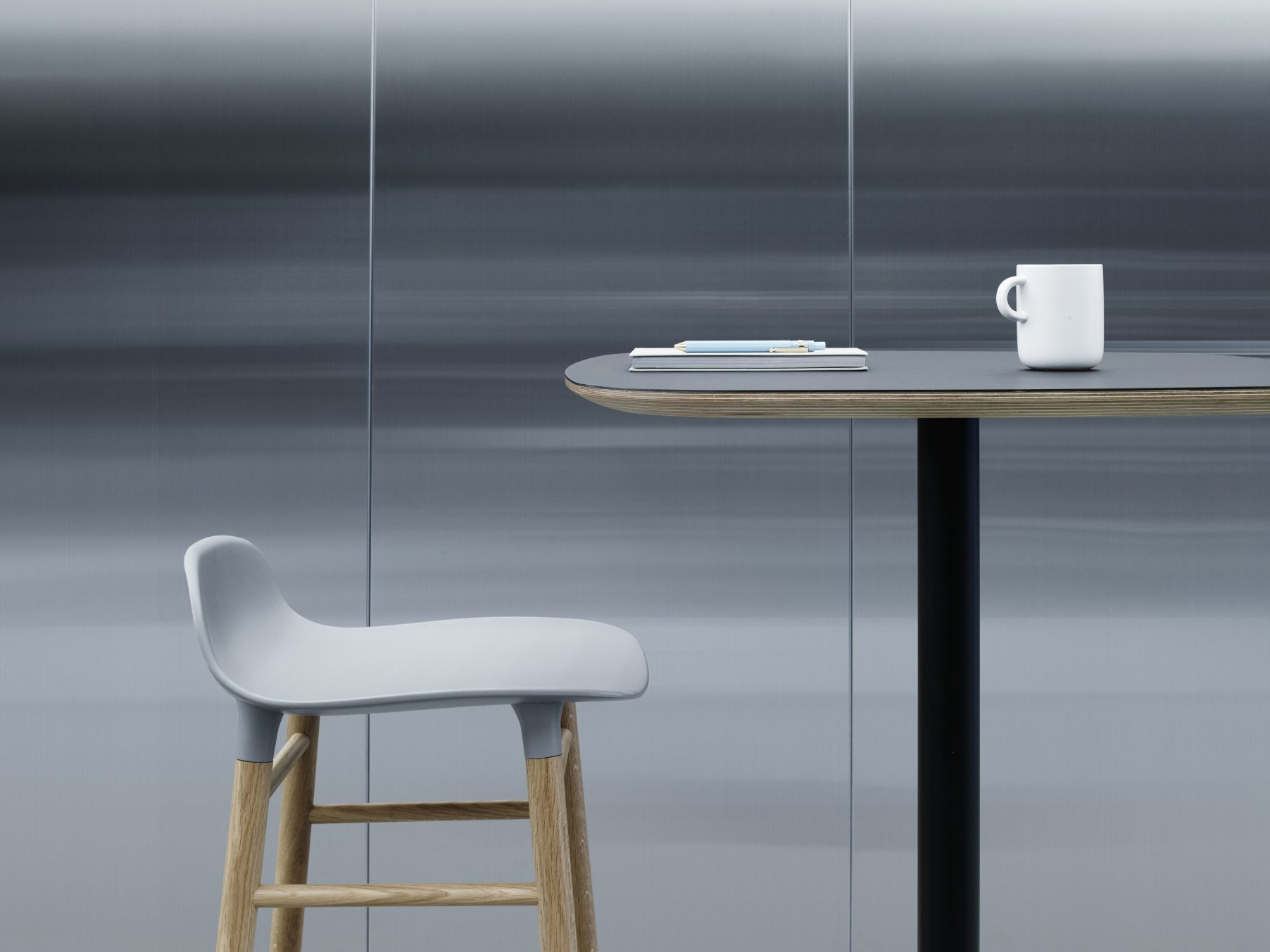 Form Barhocker von Normann Copenhagen, Hocker mit Holzbeinen und grauem Sitz an Stehtisch.