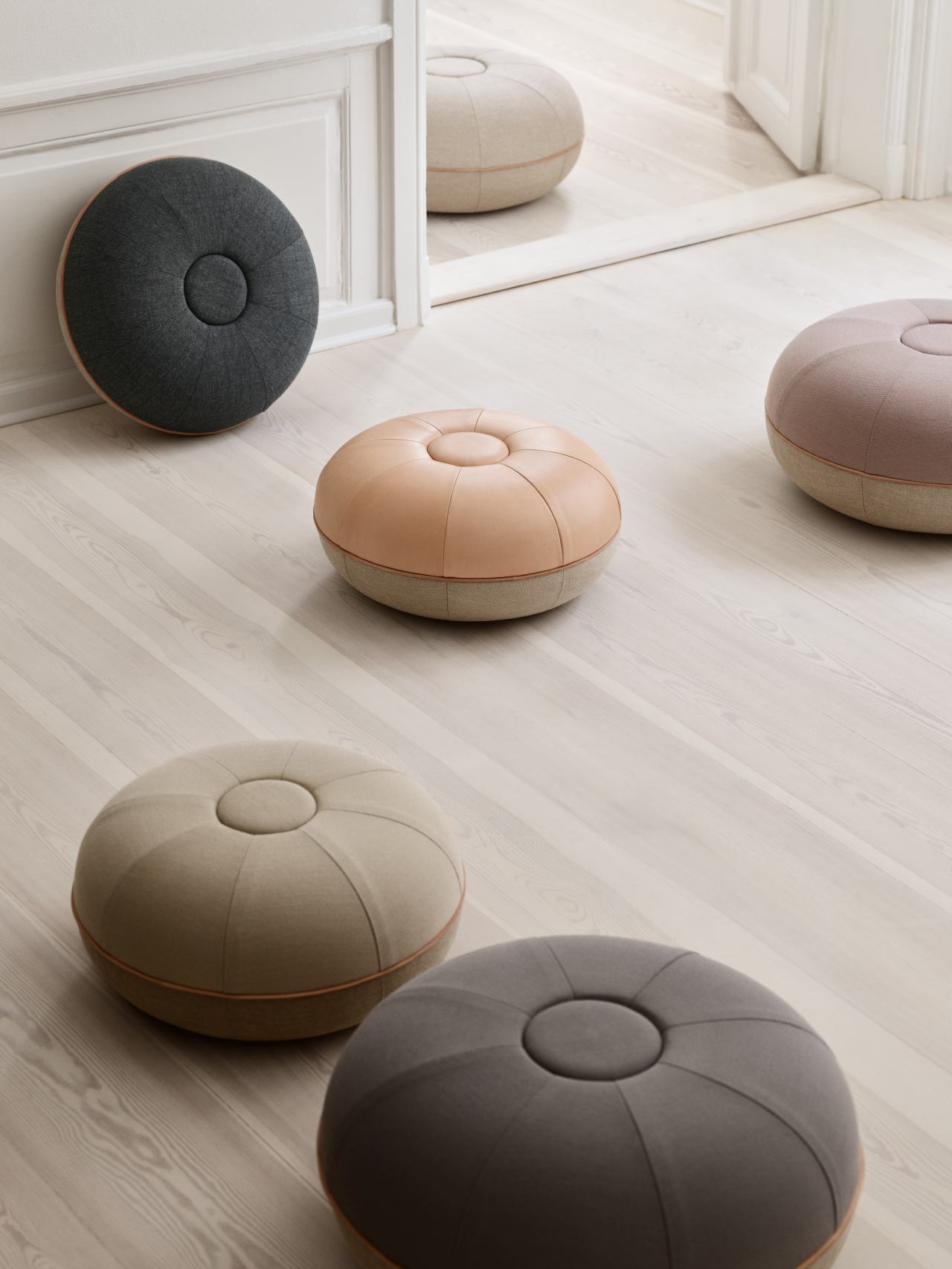 Mehrere Fritz Hansen Pouf Hocker in verschiedenen Farben auf hellem Holzboden.