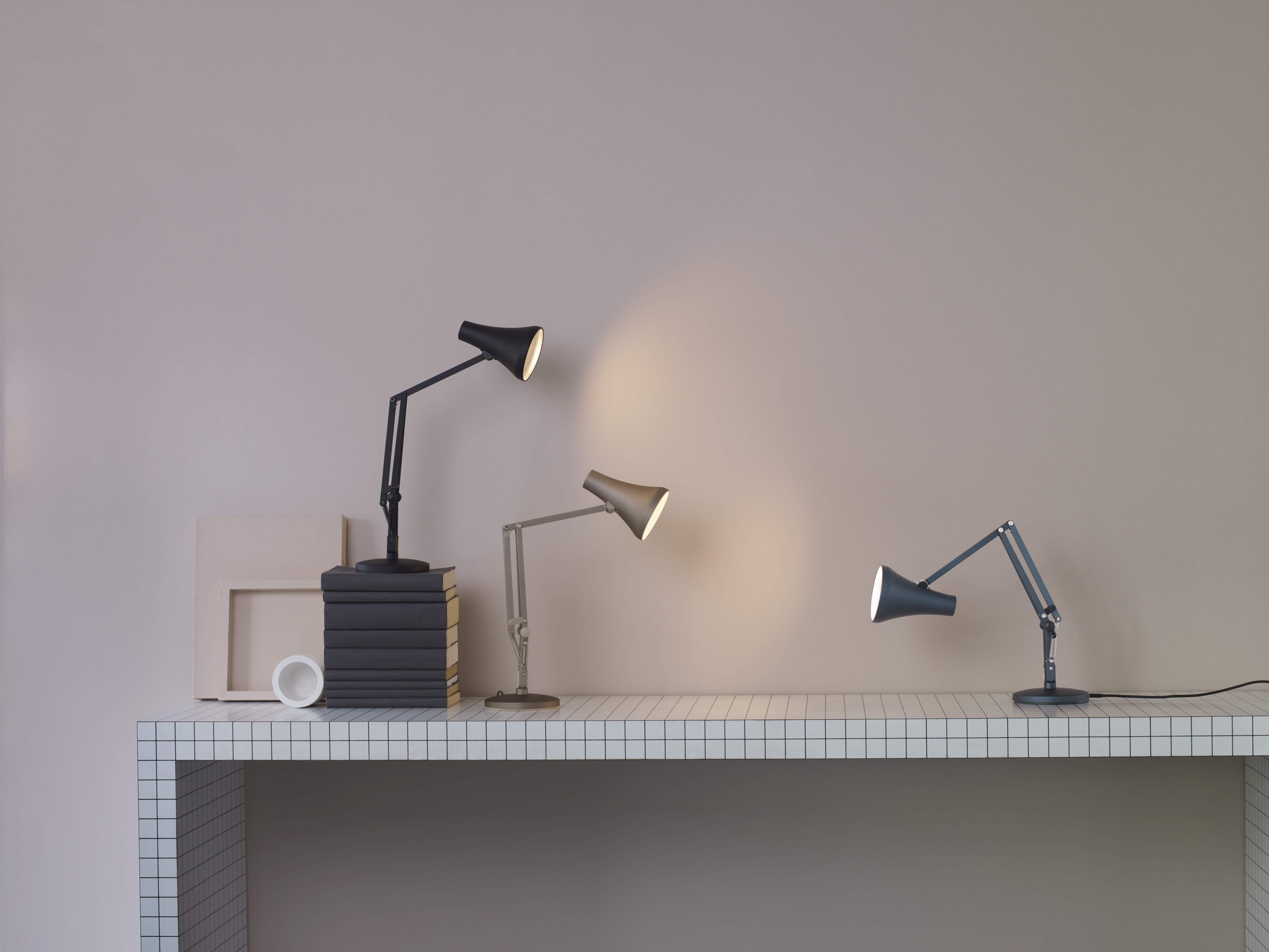 Drei moderne Schreibtischlampen in Schwarz, Grau und Blau auf einem Tisch mit Fliesenmuster.
