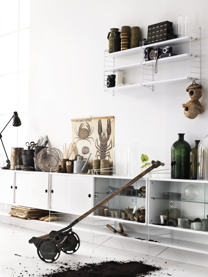 Weißes String Furniture Regalsystem im Wohnzimmer mit Dekoration und Gartengeräten.