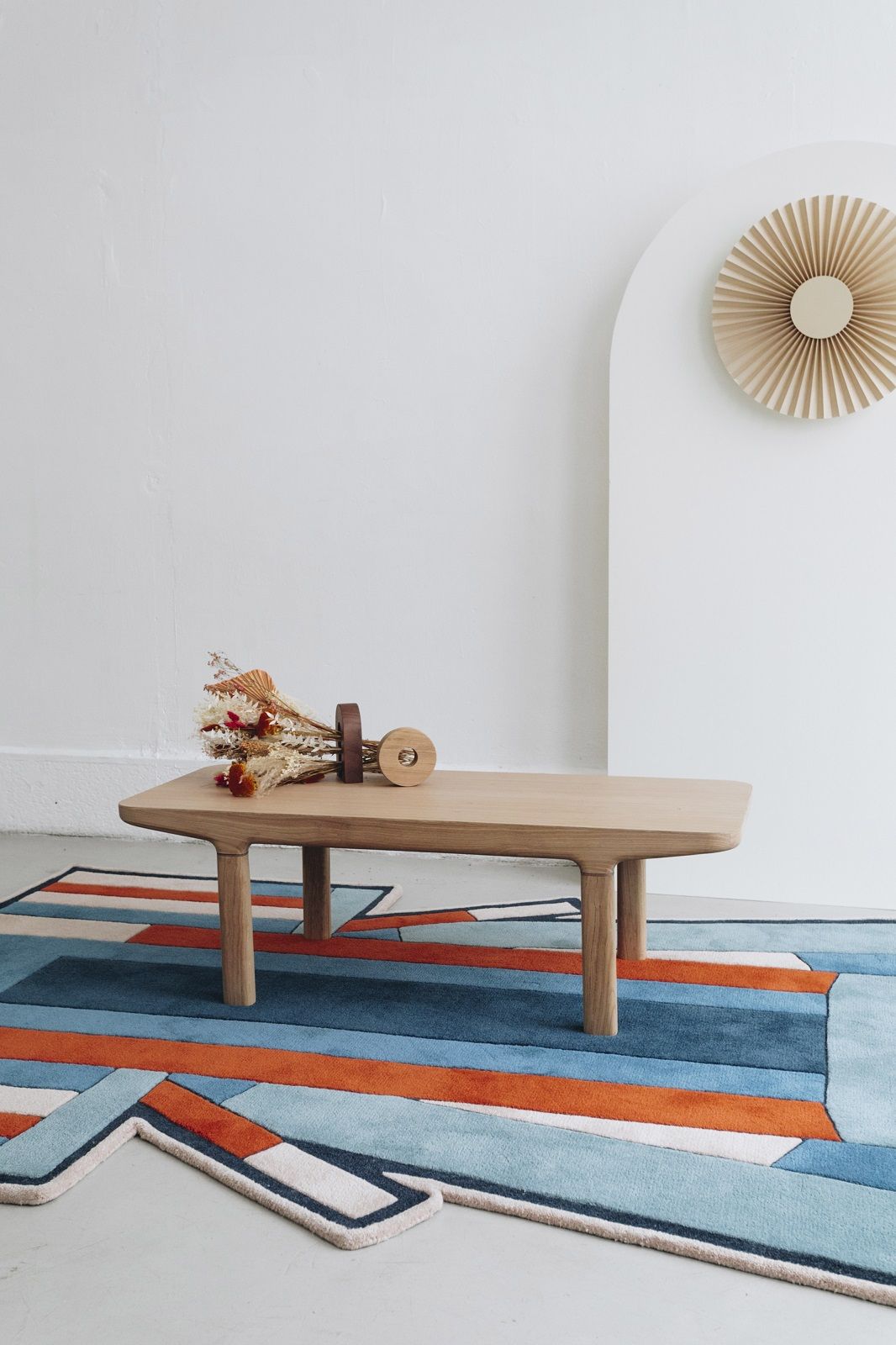 Camille Couchtisch aus hellem Holz mit Dekoration auf einem farbenfrohen Teppich.