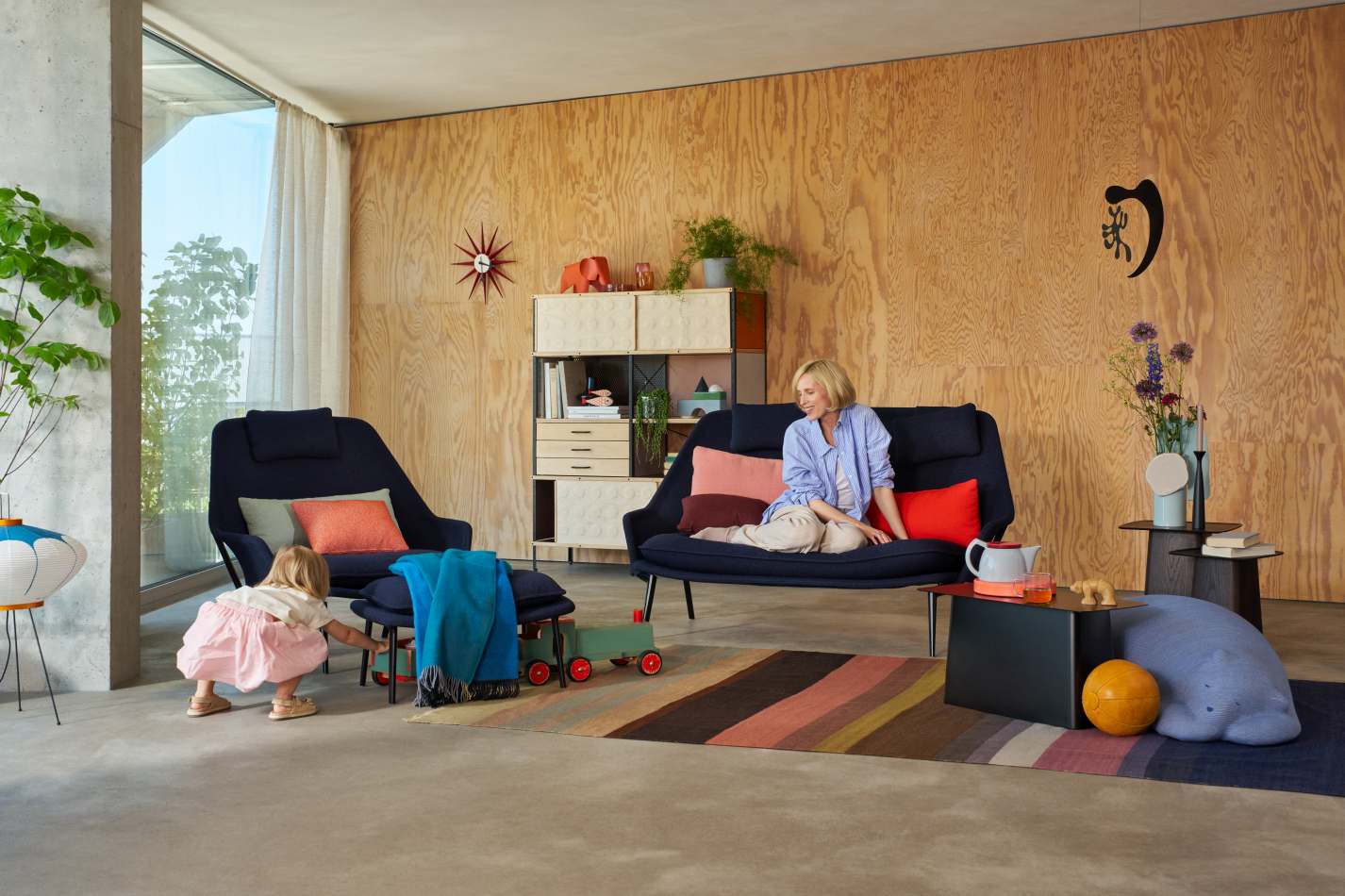 Vitra Slow Chair mit Ottoman im Wohnzimmer, Frau sitzt entspannt auf dem Sofa.