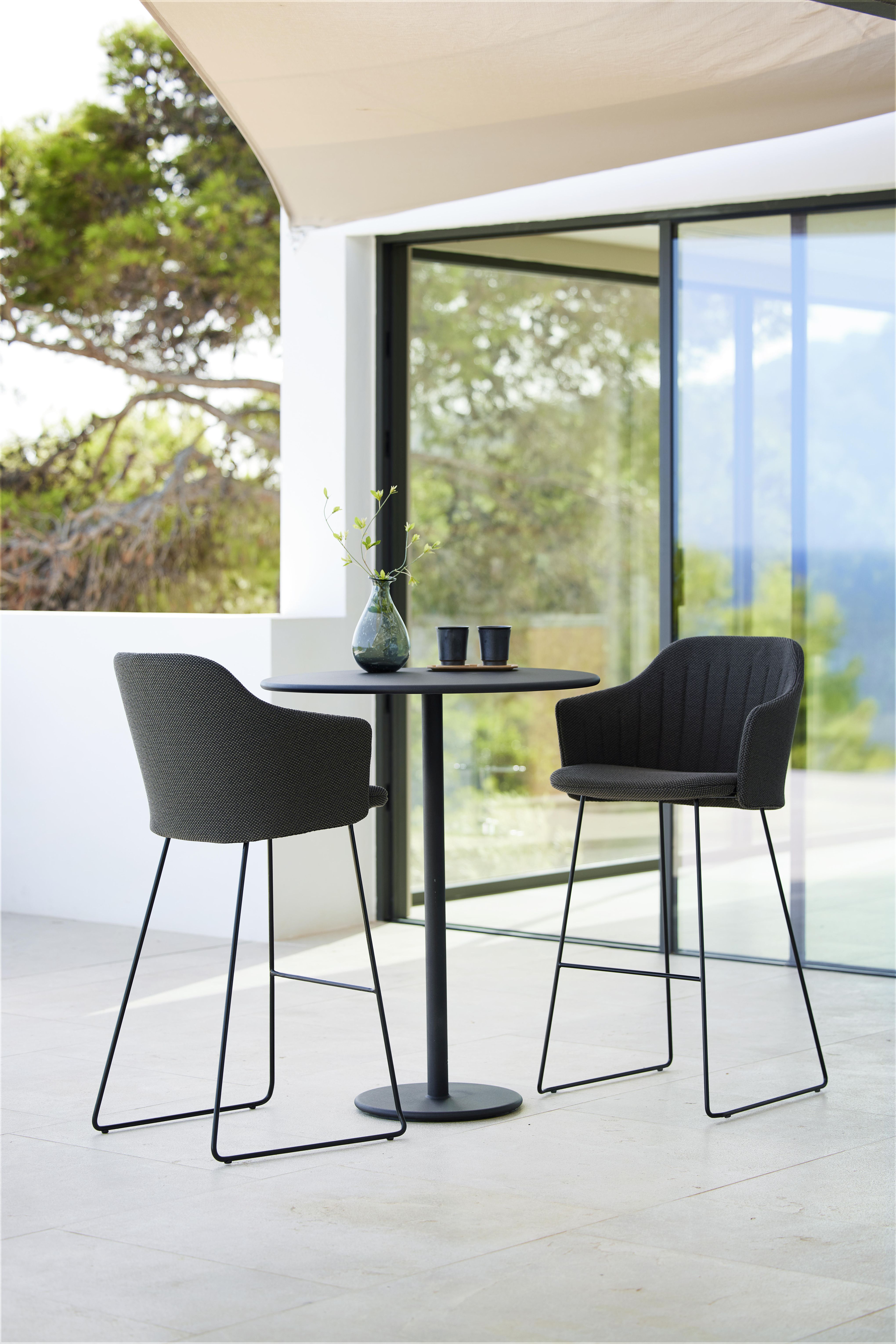 Zwei Cane-Line Choice Barhocker mit Rückenbezug und schwarzem Tisch auf einer Terrasse.