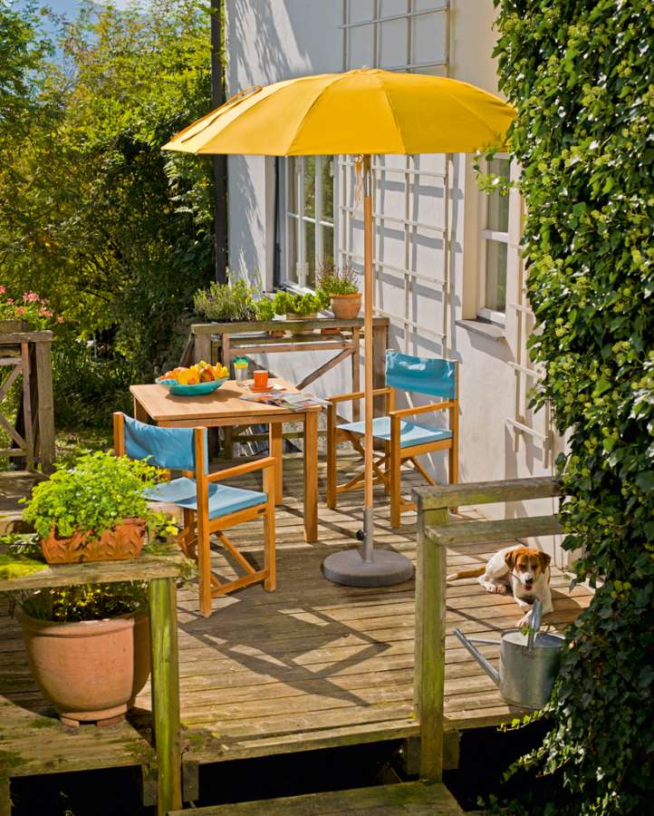 Weishäupl Cabin Sessel aus Tanne mit blauem Stoffbezug auf einer Holzterrasse mit Tisch.