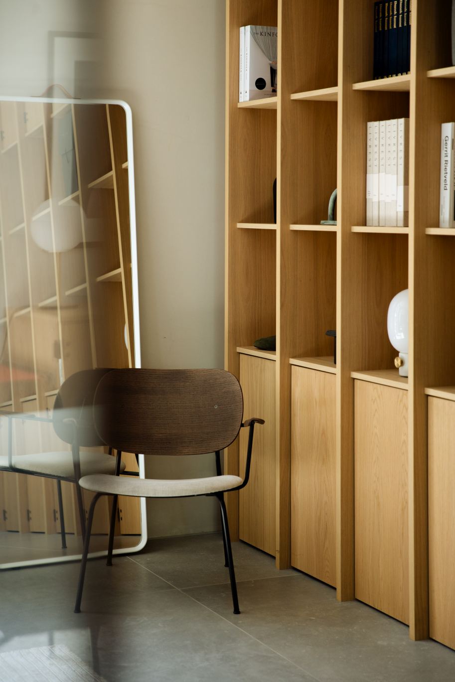 Norm Floor Mirror von Audo: Ganzkörperspiegel mit weißem Rahmen, reflektiert ein Regal im modernen Interieur.