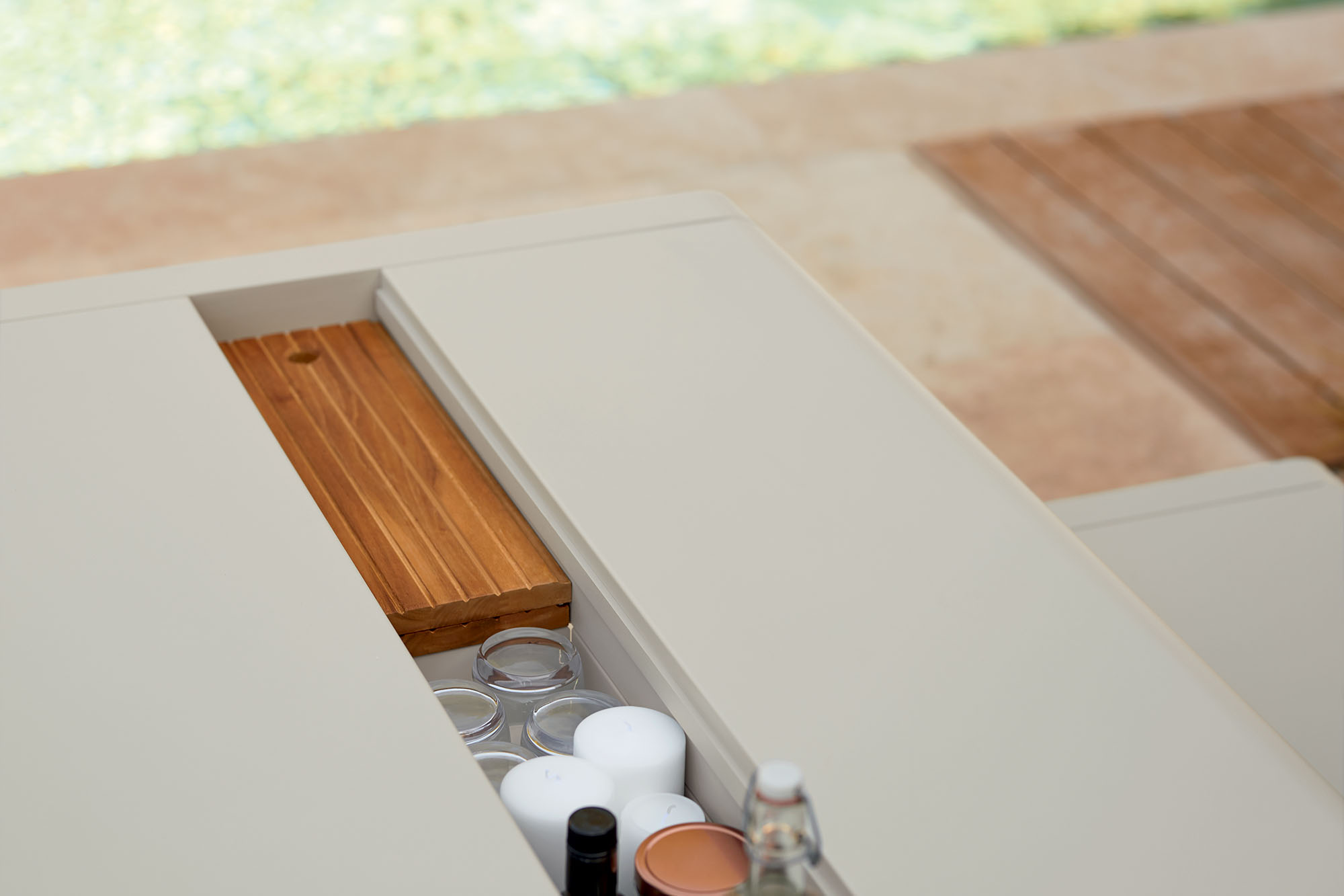 Detailaufnahme des Fermob Bellevie Outdoor Tisches mit integriertem Stauraum für Gläser, Kerzen und einer Holzplatte.