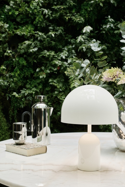 Weiße Bell Portable LED Tischleuchte von Tom Dixon auf einem Tisch im Freien.