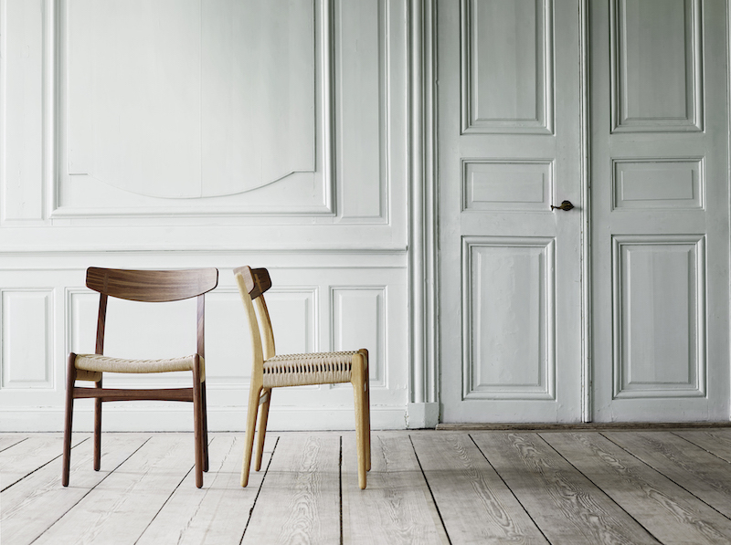 Zwei CH23 Holzstühle von Carl Hansen & Søn mit geflochtenen Sitzen vor weißer Wand.