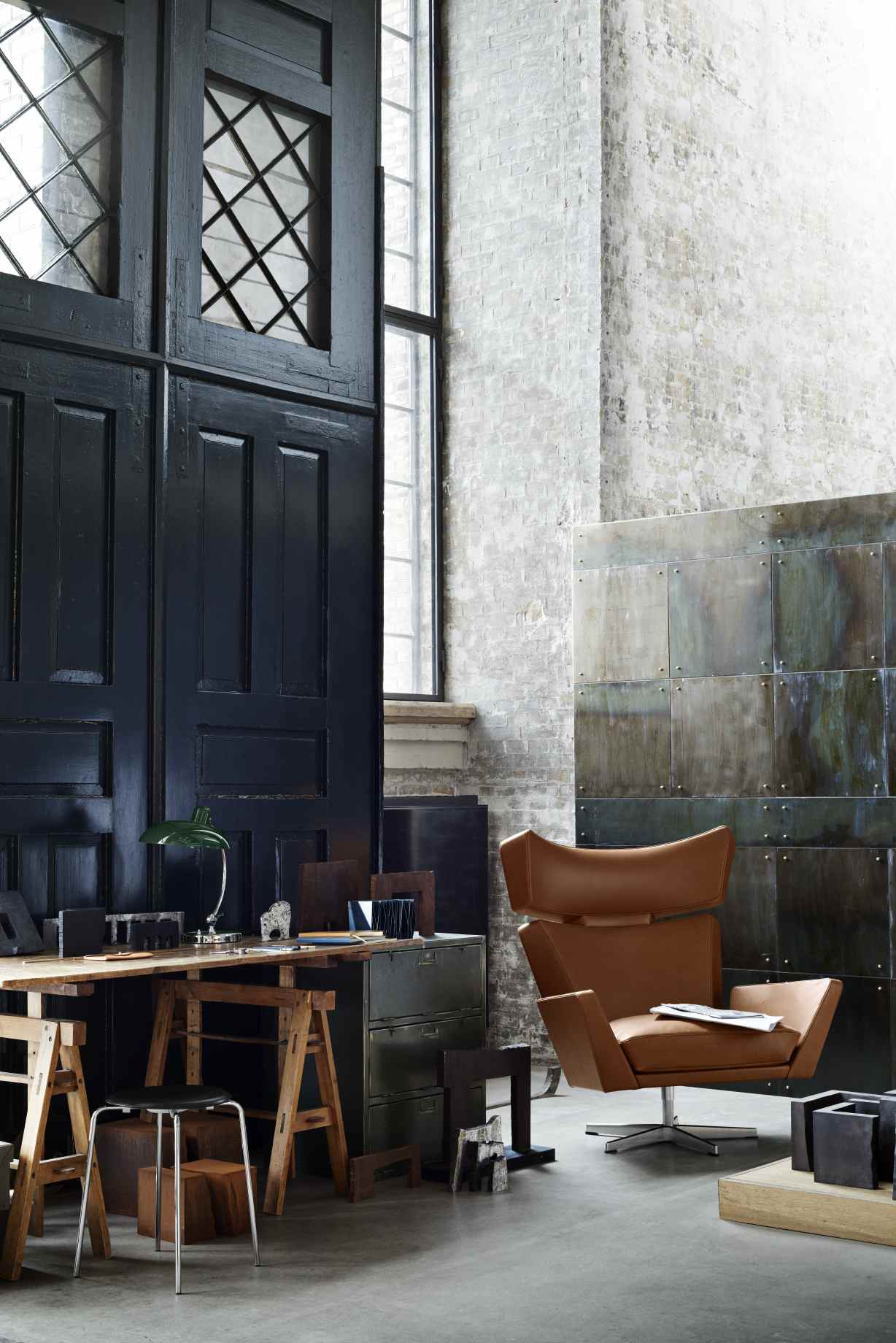 Oksen Sessel von Fritz Hansen in braunem Leder vor industriellem Hintergrund.