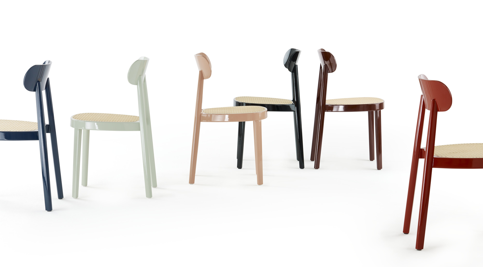 Mehrere Thonet 118 Holzstühle in verschiedenen Farben mit Wiener Geflecht Sitzfläche auf weißem Hintergrund.