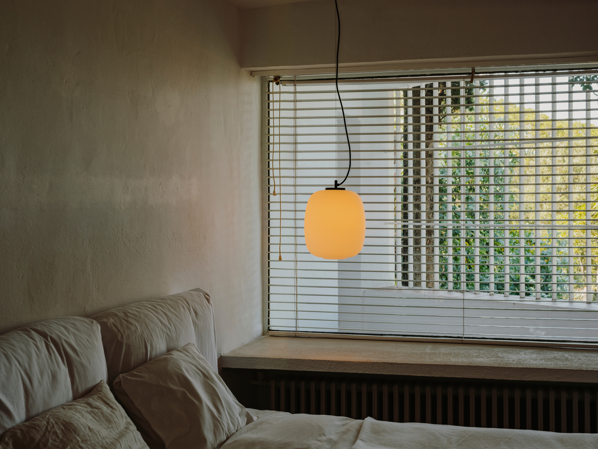 Globo Cesta Pendelleuchte von Santa & Cole über Bett mit Fenster im Hintergrund.