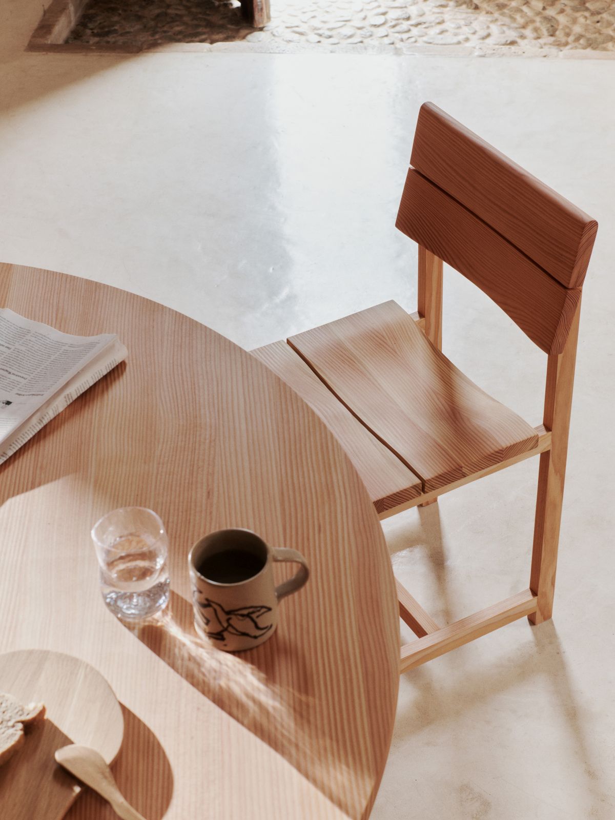 Ferm Living Visit Esszimmerstuhl aus hellem Holz neben einem runden Esstisch mit Geschirr.