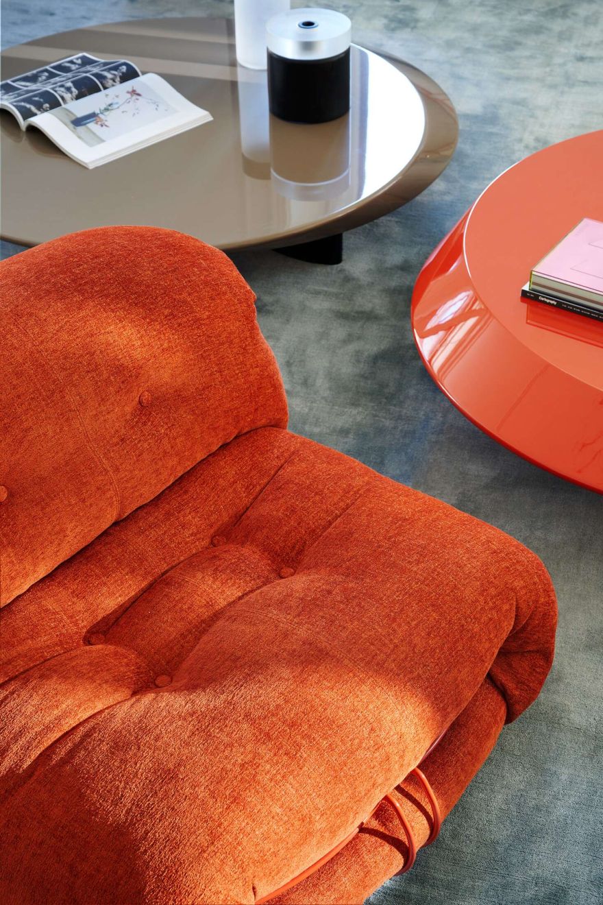 Detailaufnahme des orangefarbenen Cassina Soriana Sessels mit Knopfheftung, ergänzt durch moderne Couchtische im Wohnzimmer.