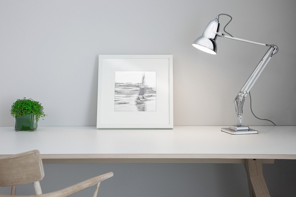 Schreibtisch mit Chrom-Schreibtischlampe, gerahmtem Segelboot-Bild und grüner Pflanze für modernes Homeoffice.