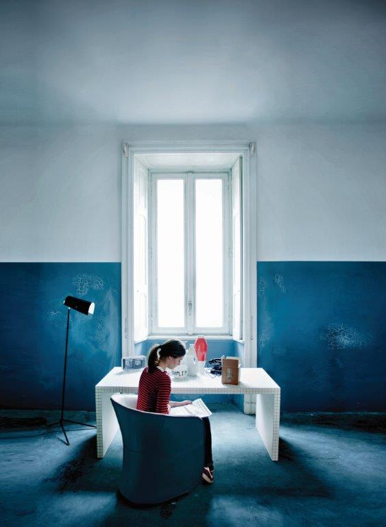 Frau liest im blauen Calla Sessel von Zanotta am Schreibtisch in blauem Raum.