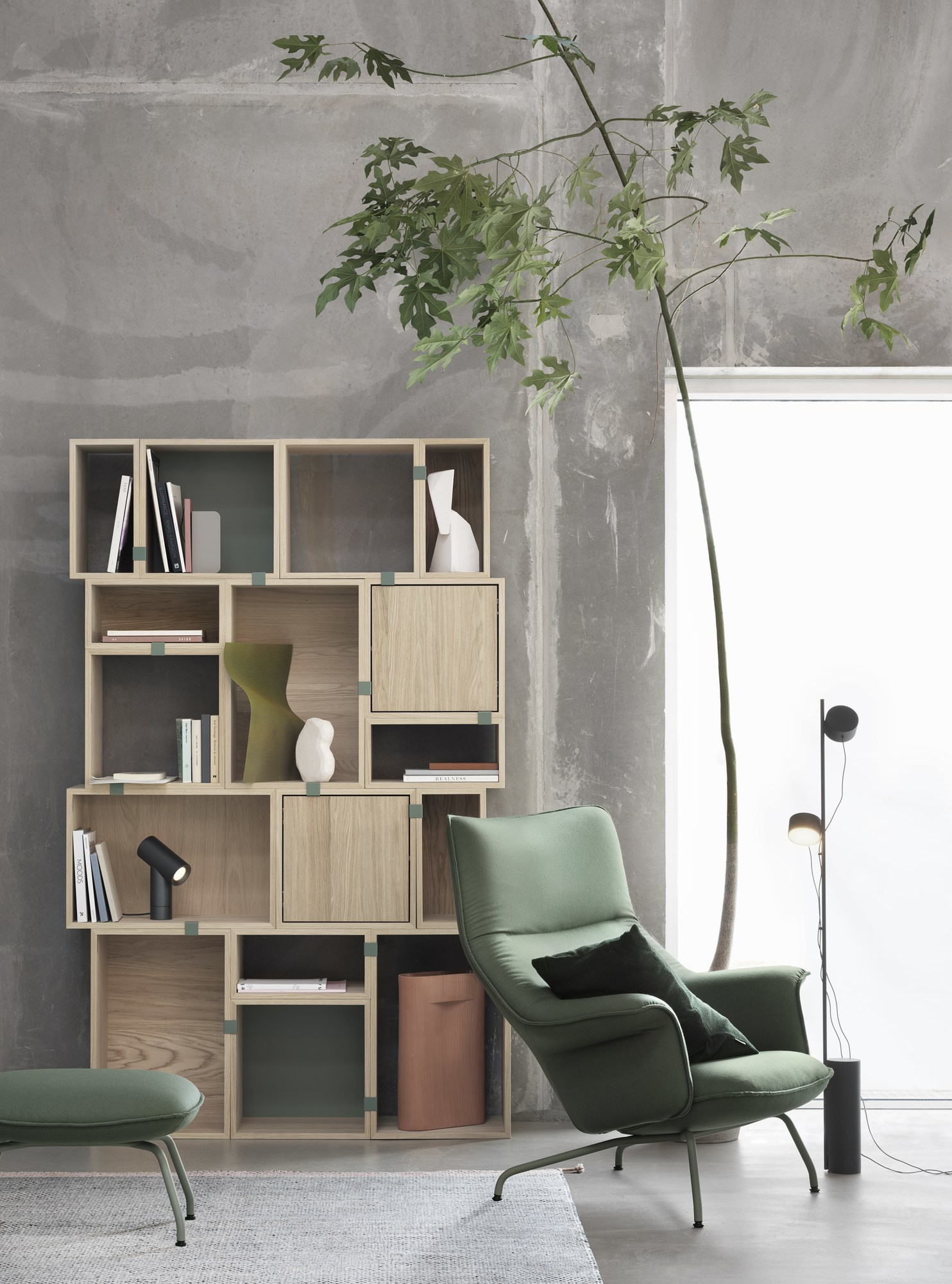 Muuto Doze Sessel mit Ottoman in Grün vor Bücherregal und Stehlampe.