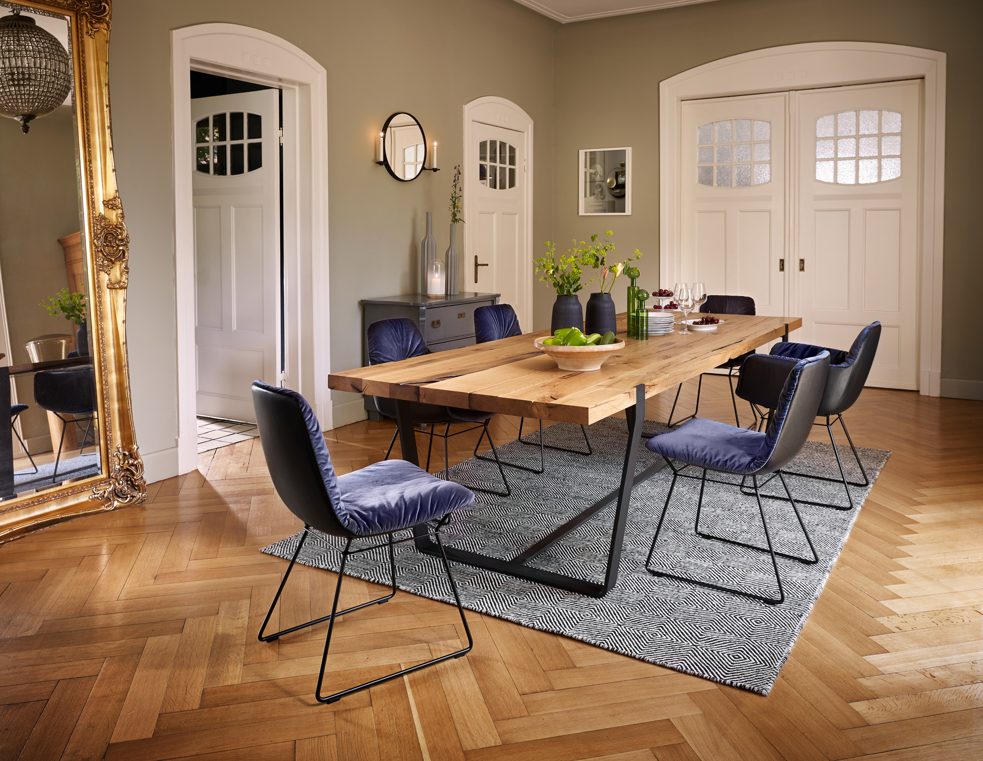 Esszimmer mit Holztisch, Leya Stühlen von Freifrau Manufaktur mit blauem Samtbezug und modernem Teppich.