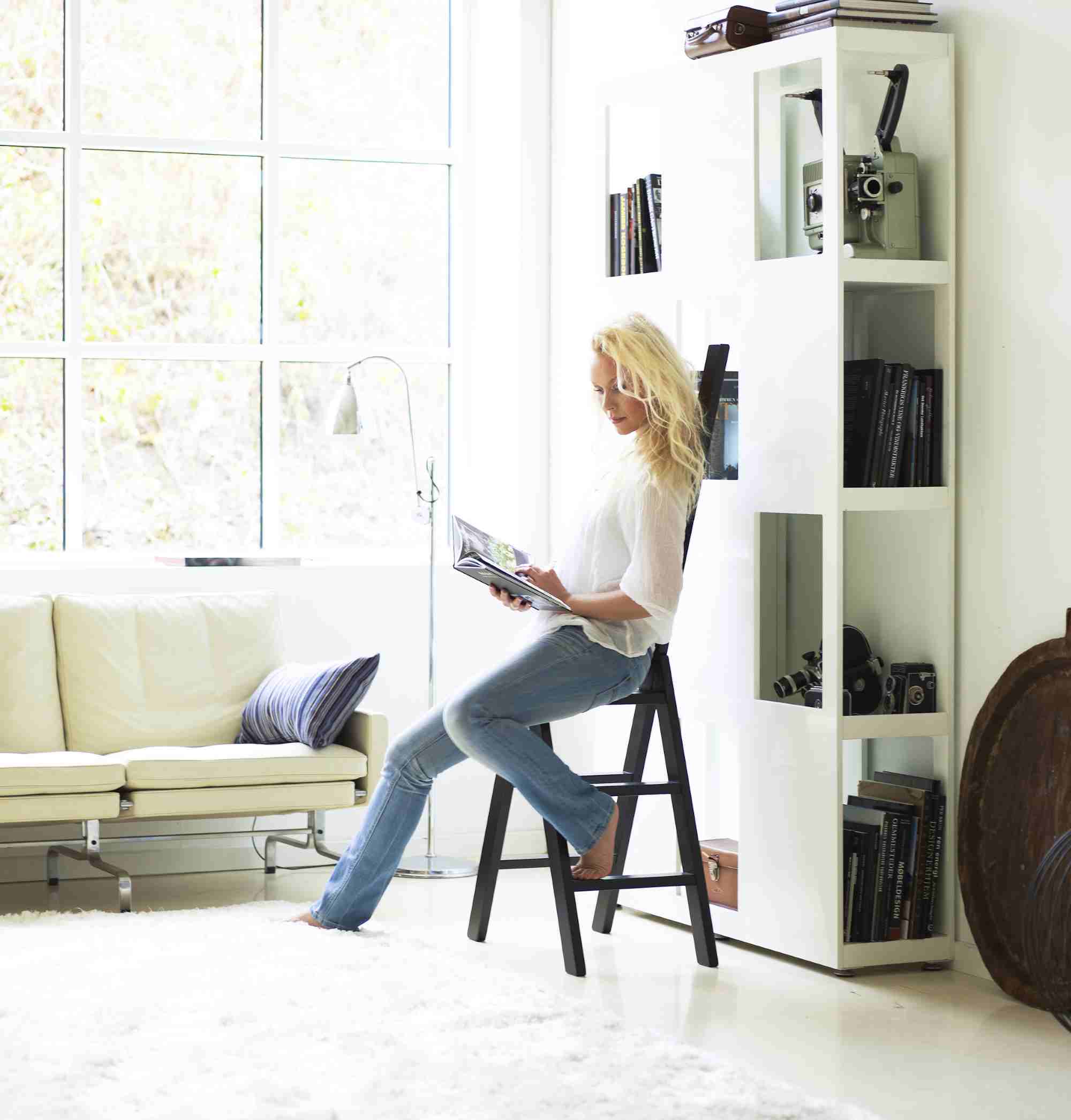 Frau liest auf der Hindevadgaard Trittleiter in modernem Wohnzimmer mit Sofa und Bücherregal.