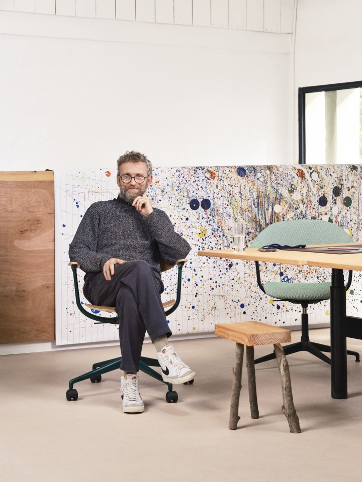 Mann sitzt entspannt auf dem Vitra Mynt Bürodrehstuhl mit Kunststoffrücken und Holzsitzfläche.