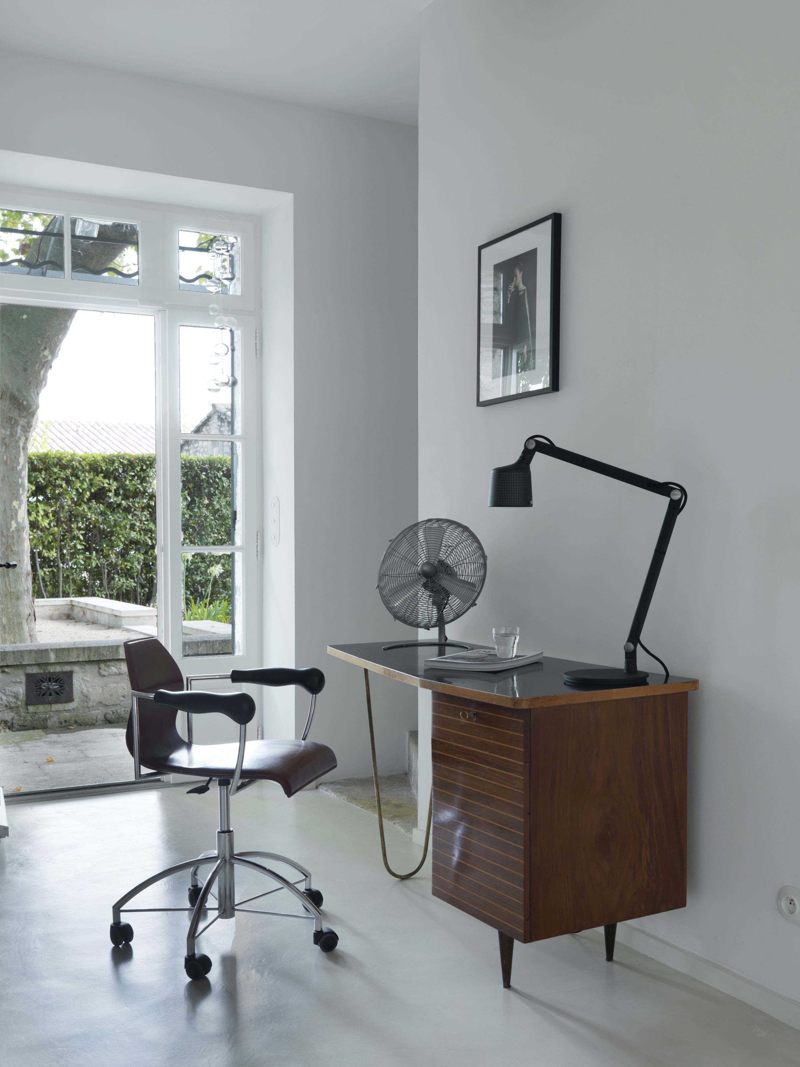 Schwarze Vipp Tischlampe auf Schreibtisch mit Ventilator und Bürostuhl in modernem, hellen Arbeitszimmer.