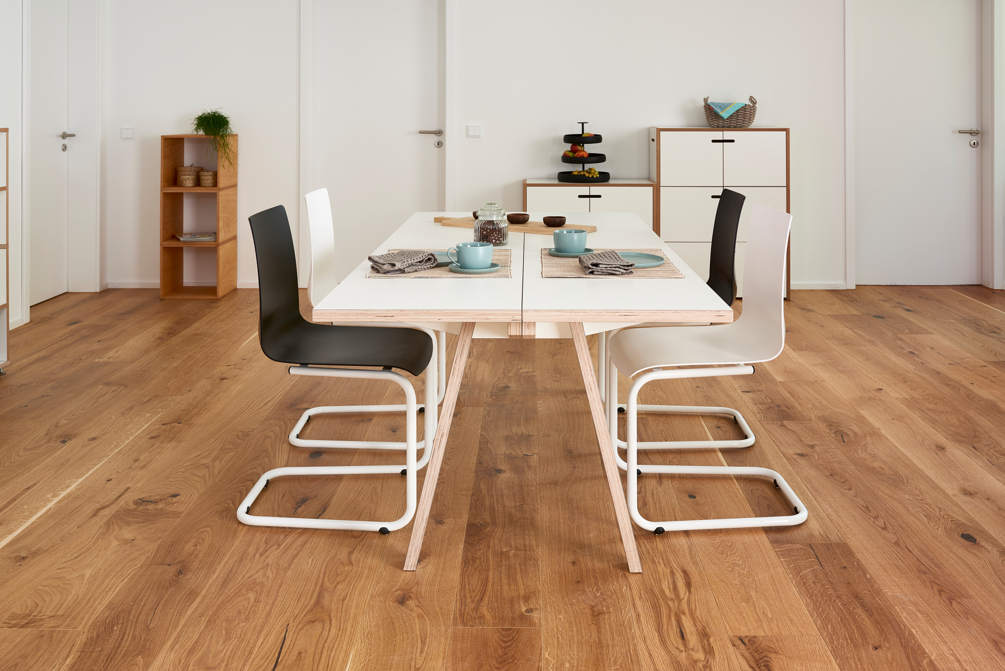 Tojo Steck Tisch aus Holz mit weißer Tischplatte und schwarzen und weißen Stühlen.