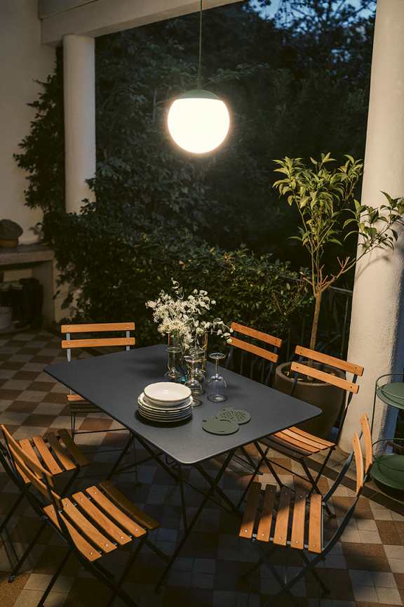 Außenbereich mit Esstisch und Stühlen, beleuchtet durch eine moderne Mooon Pendelleuchte von Fermob.