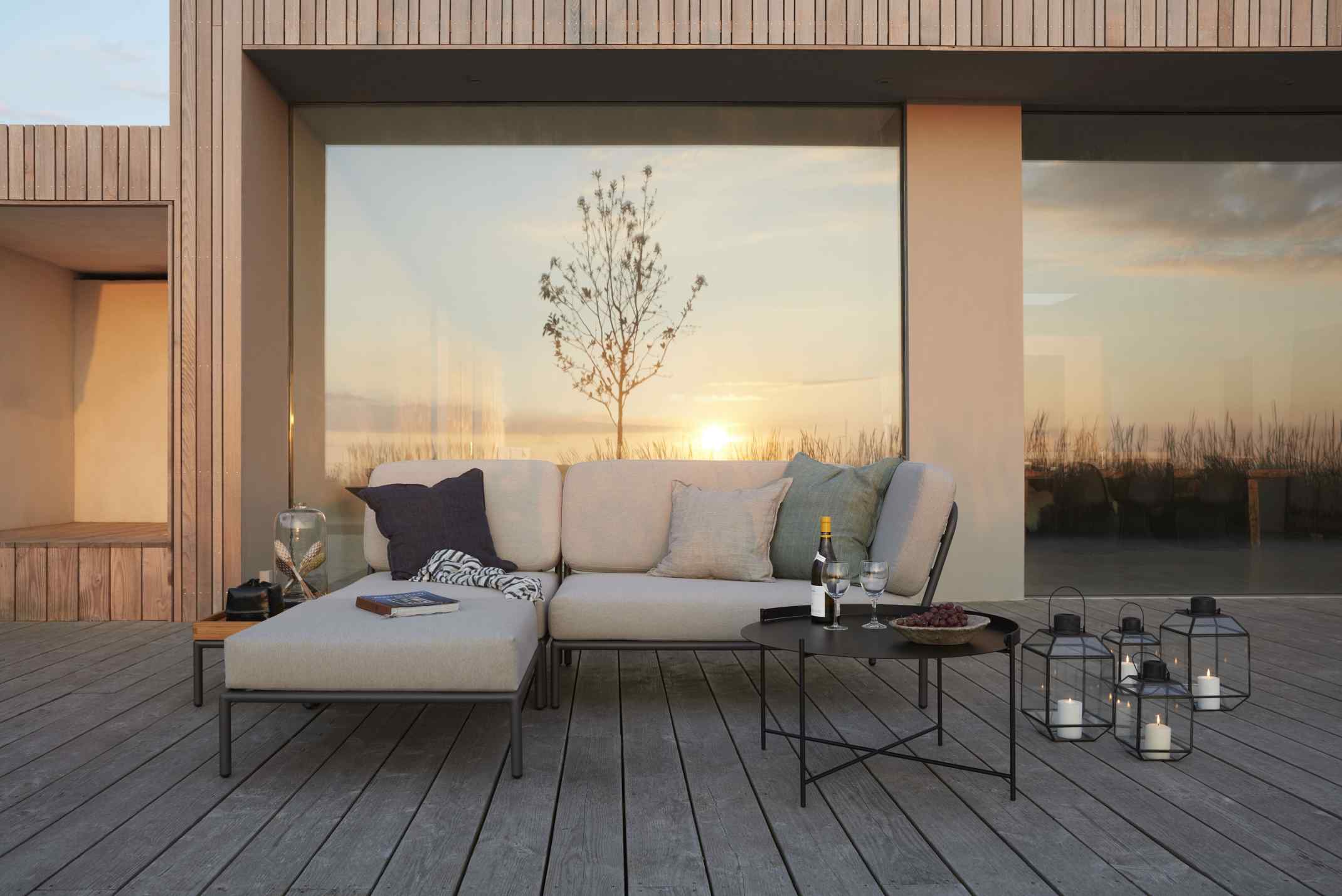 Level Sofa Outdoor von Houe auf Holzterrasse mit Tisch, Windlichtern und Blick auf den Sonnenuntergang.