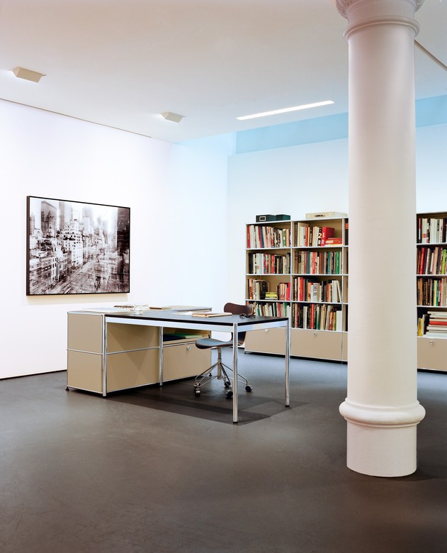USM Haller Tisch 150x75 in stilvollem Büroambiente mit Bücherregal und moderner Dekoration.