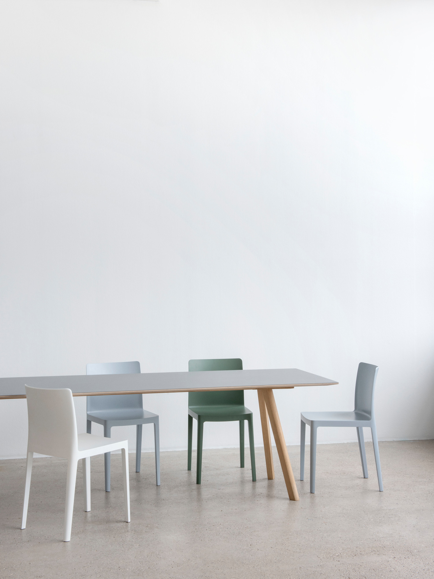 Copenhague Table CPH 30 Esstisch von Hay mit grauer Tischplatte und Holzbeinen, umgeben von Stühlen.